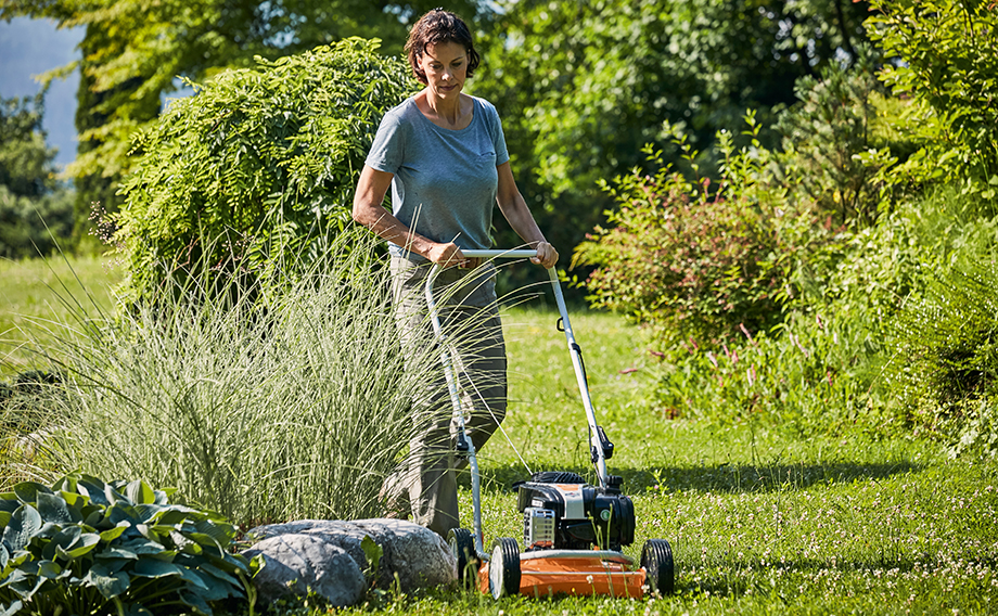 Een vrouw maait het gazon in een tuin met een STIHL RM 2 R-mulchmaaier