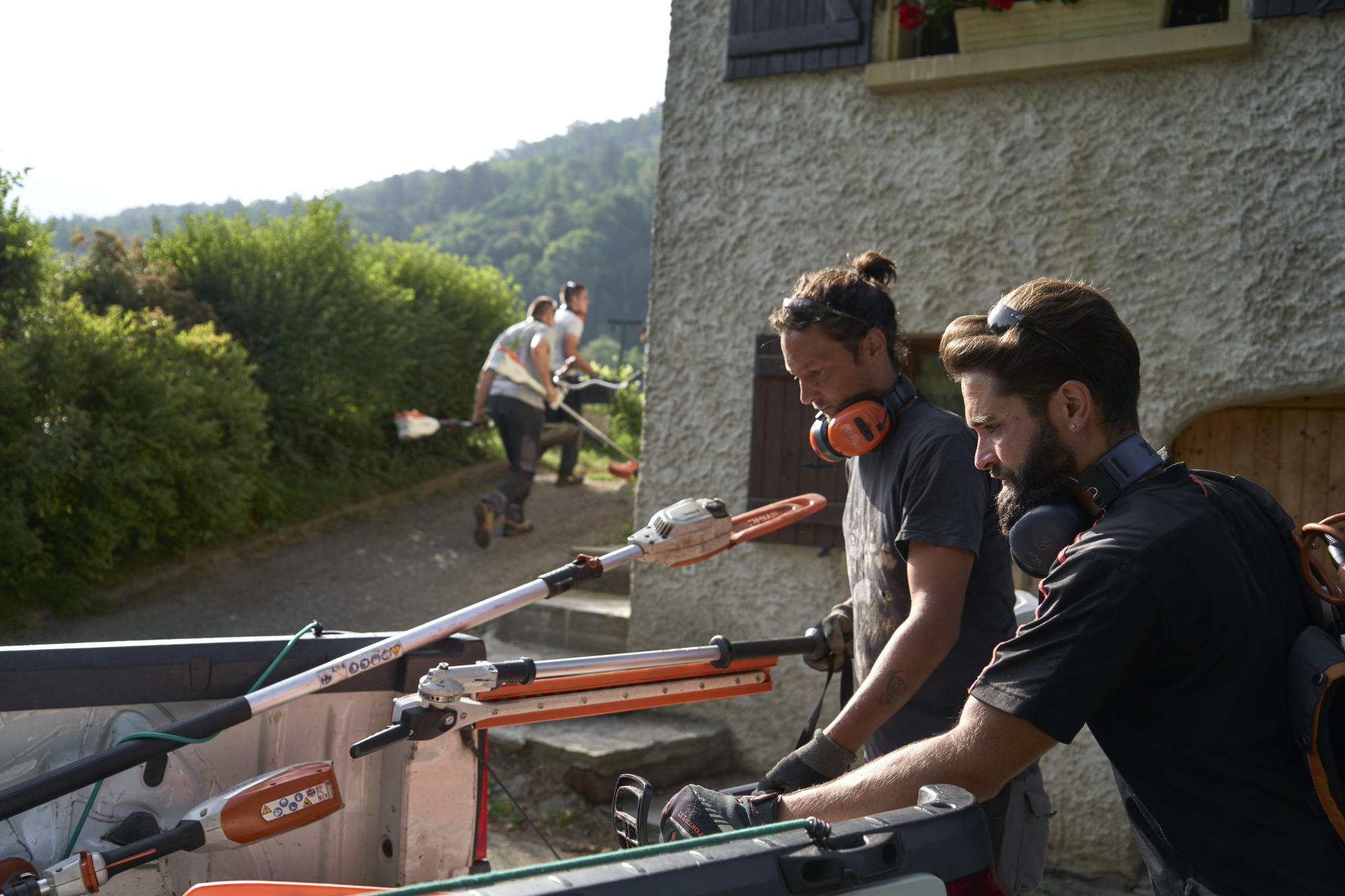 Twee landschapsarchitecten lossen STIHL accumachines uit een auto, op de achtergrond staan andere hoveniers 