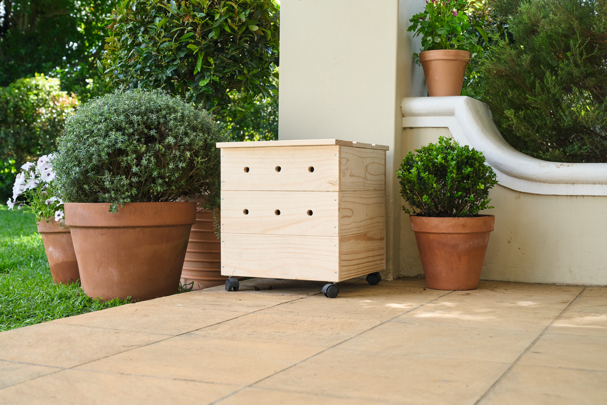 Une terrasse en carrelage avec un vermicomposteur en bois fait maison, entouré de plantes en pot