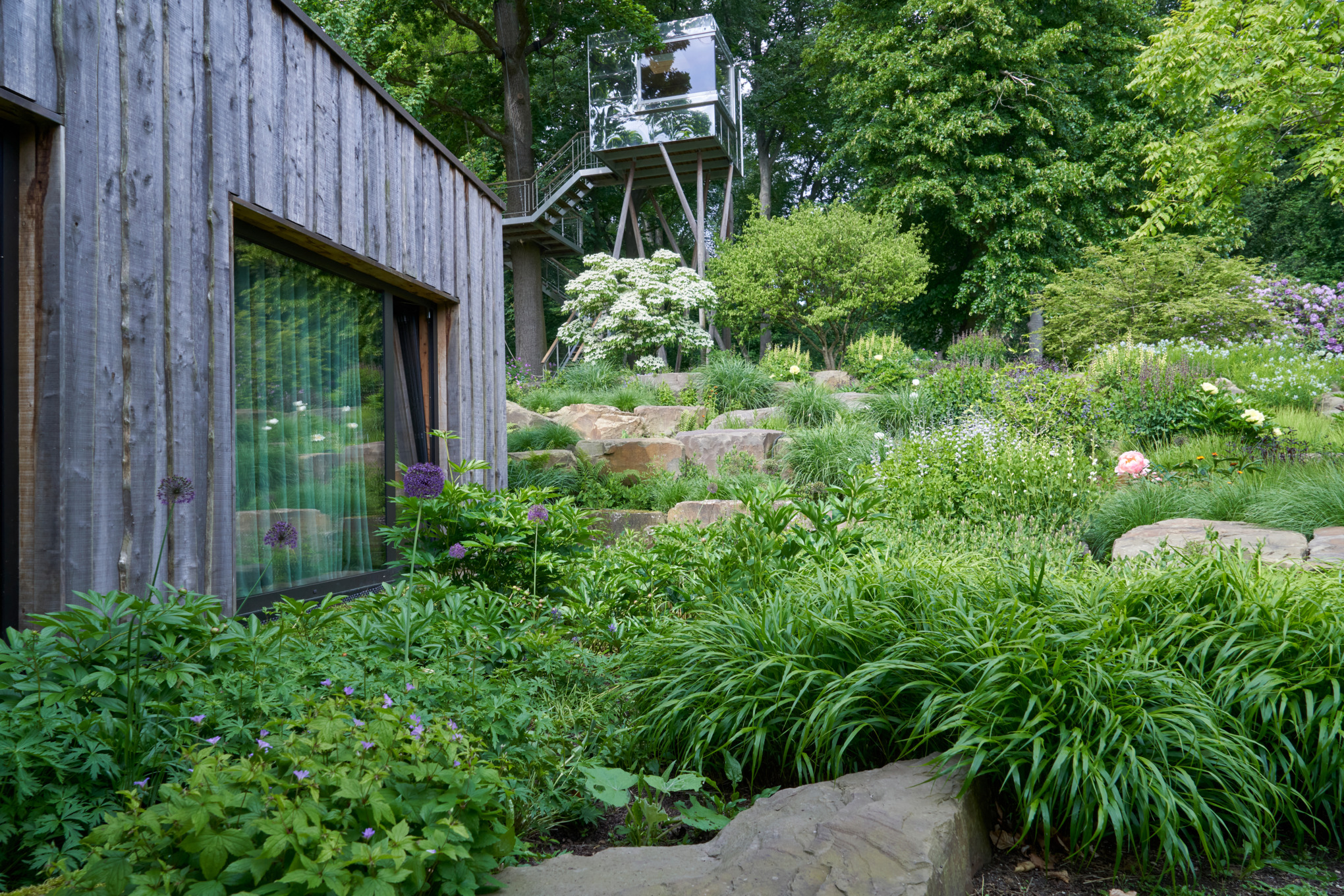 Un jardin en pente avec des pierres près d’une maison en bois, avec un point de vue en arrière-plan