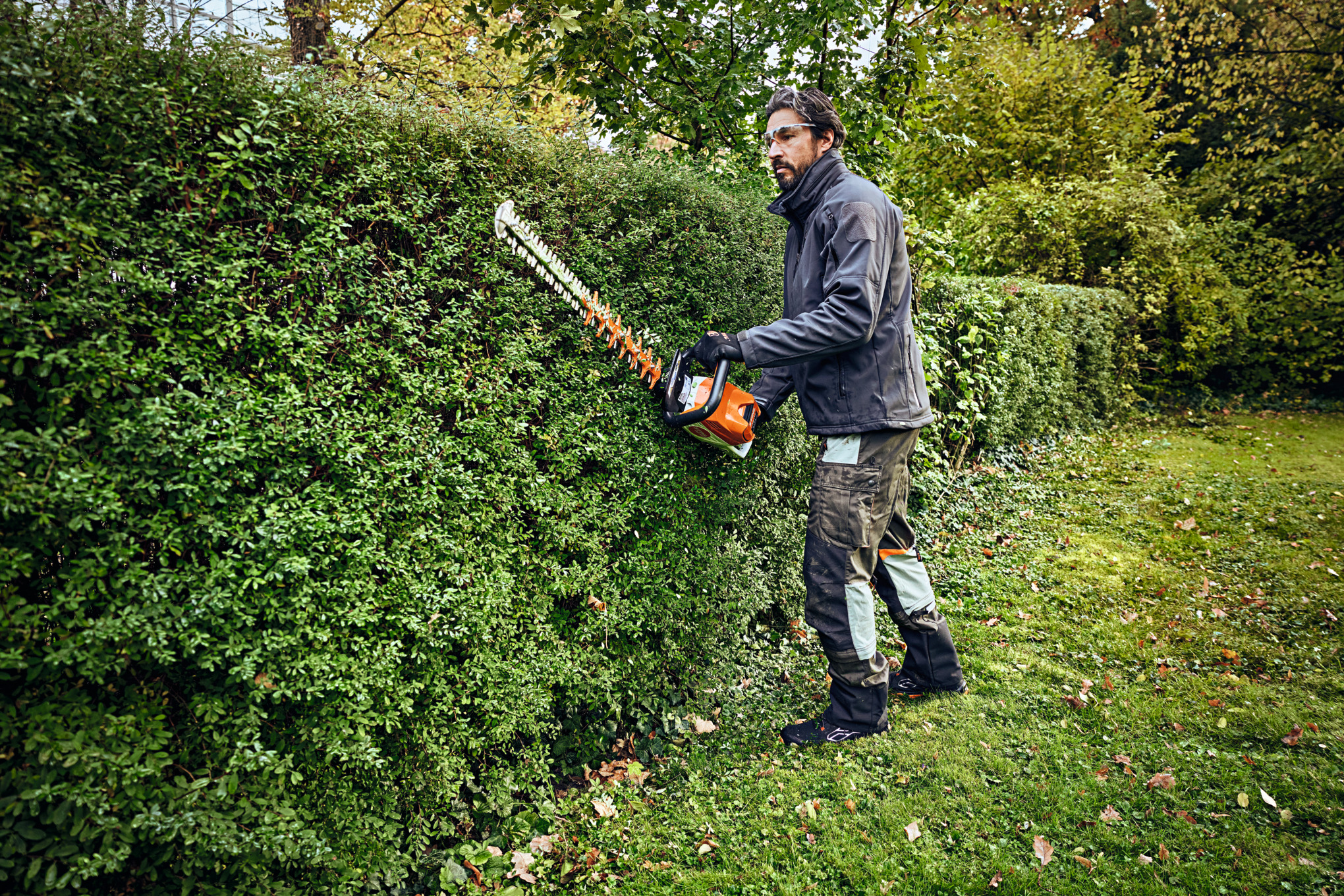 Un homme en équipement de protection taille une haie avec un taille-haie STIHL 