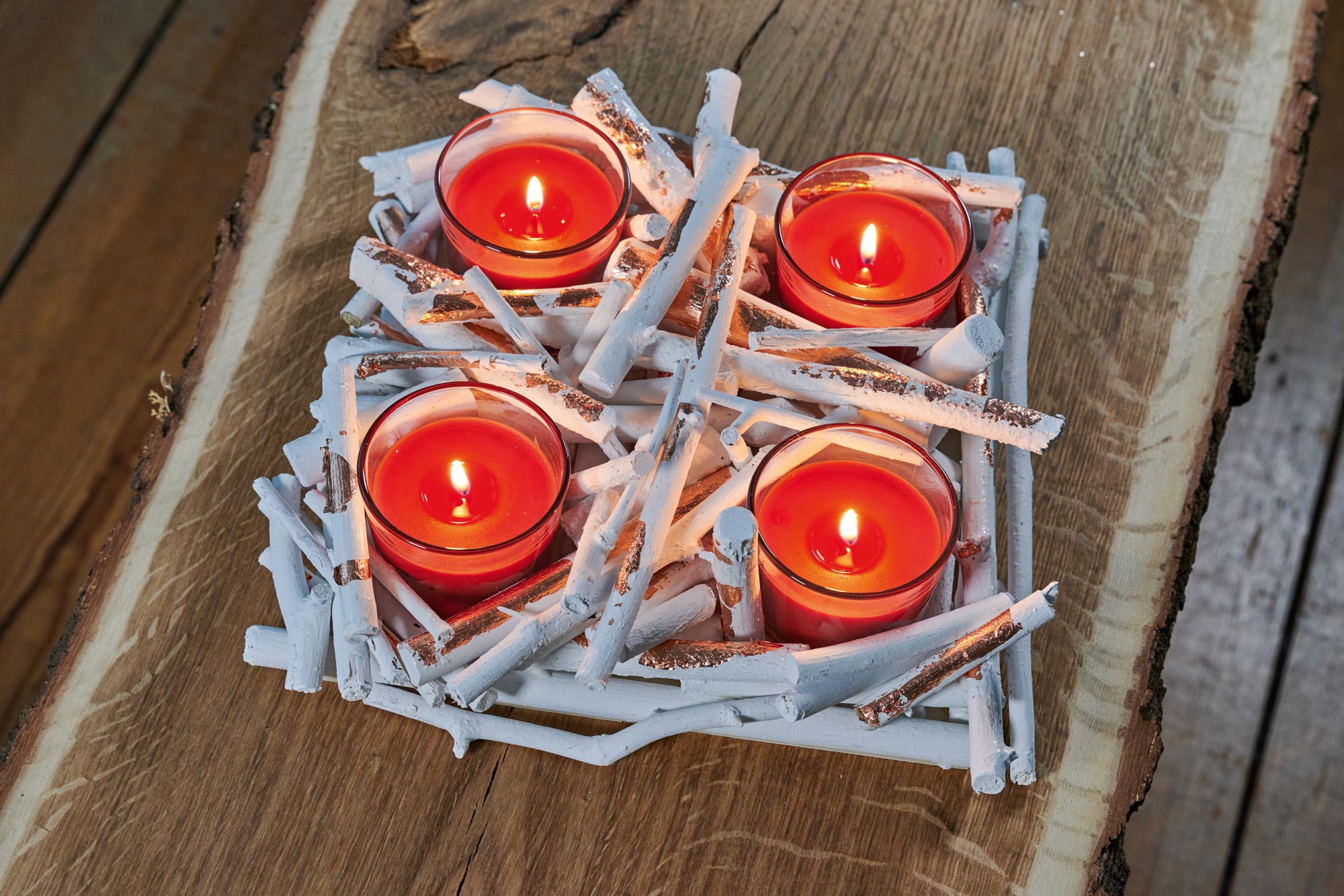 Vier rode kaarsen in glazen branden in een zelfgemaakte adventskrans van takjes