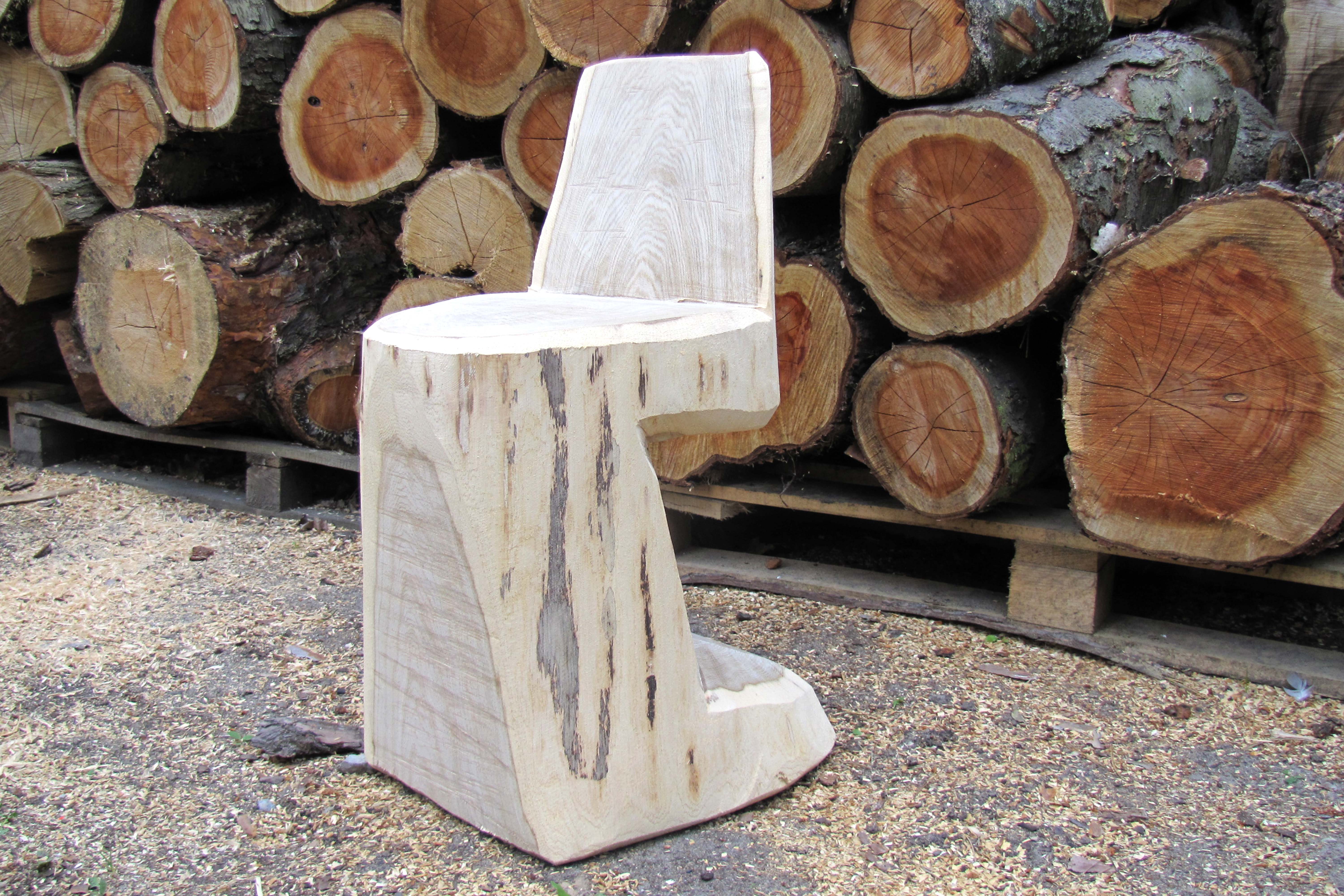 Zelfgemaakte houten stoel vóór een stapel boomstammen