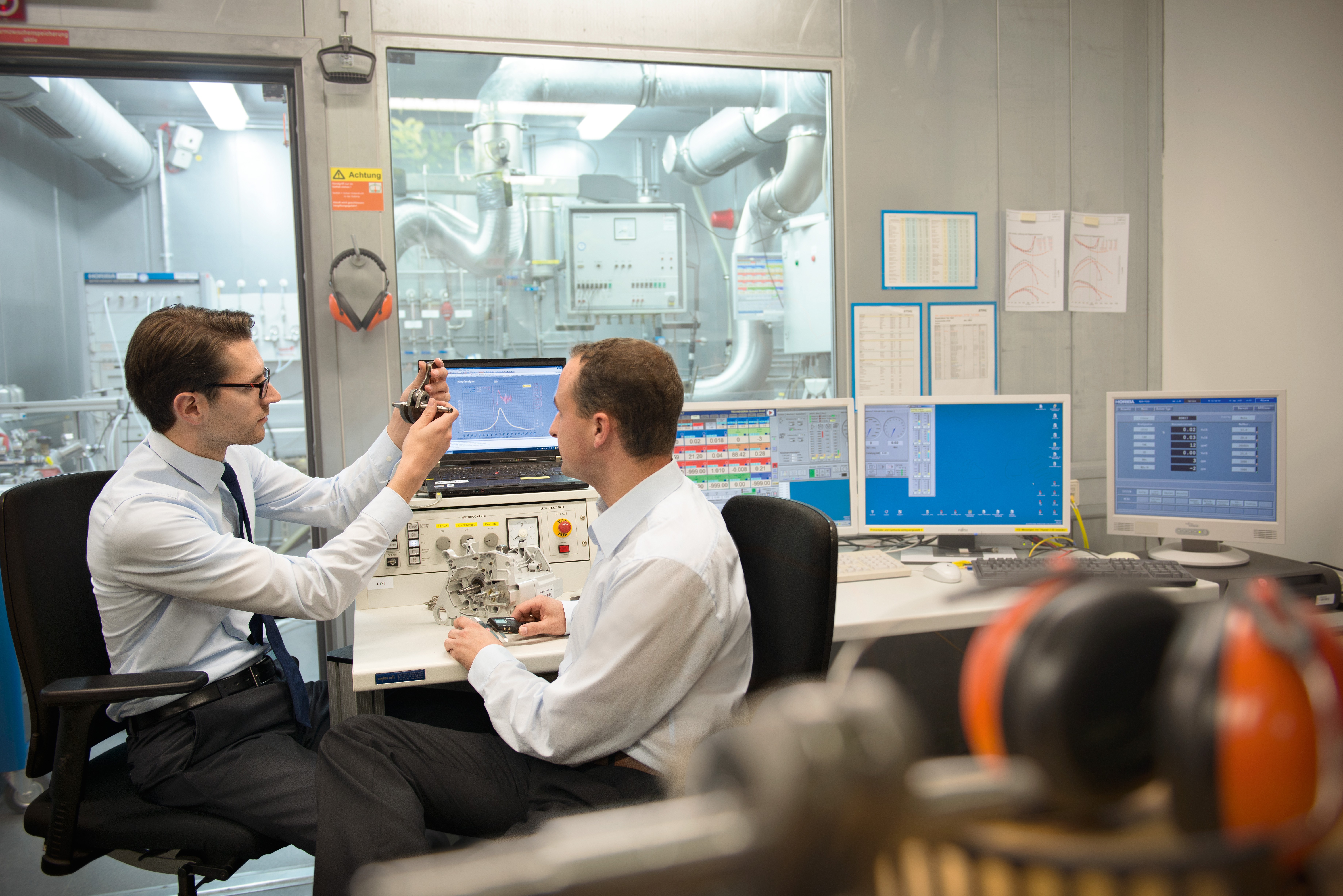 Twee mannen bestuderen in een laboratorium aan een bureau met meerdere schermen een onderdeel voor een nieuw product