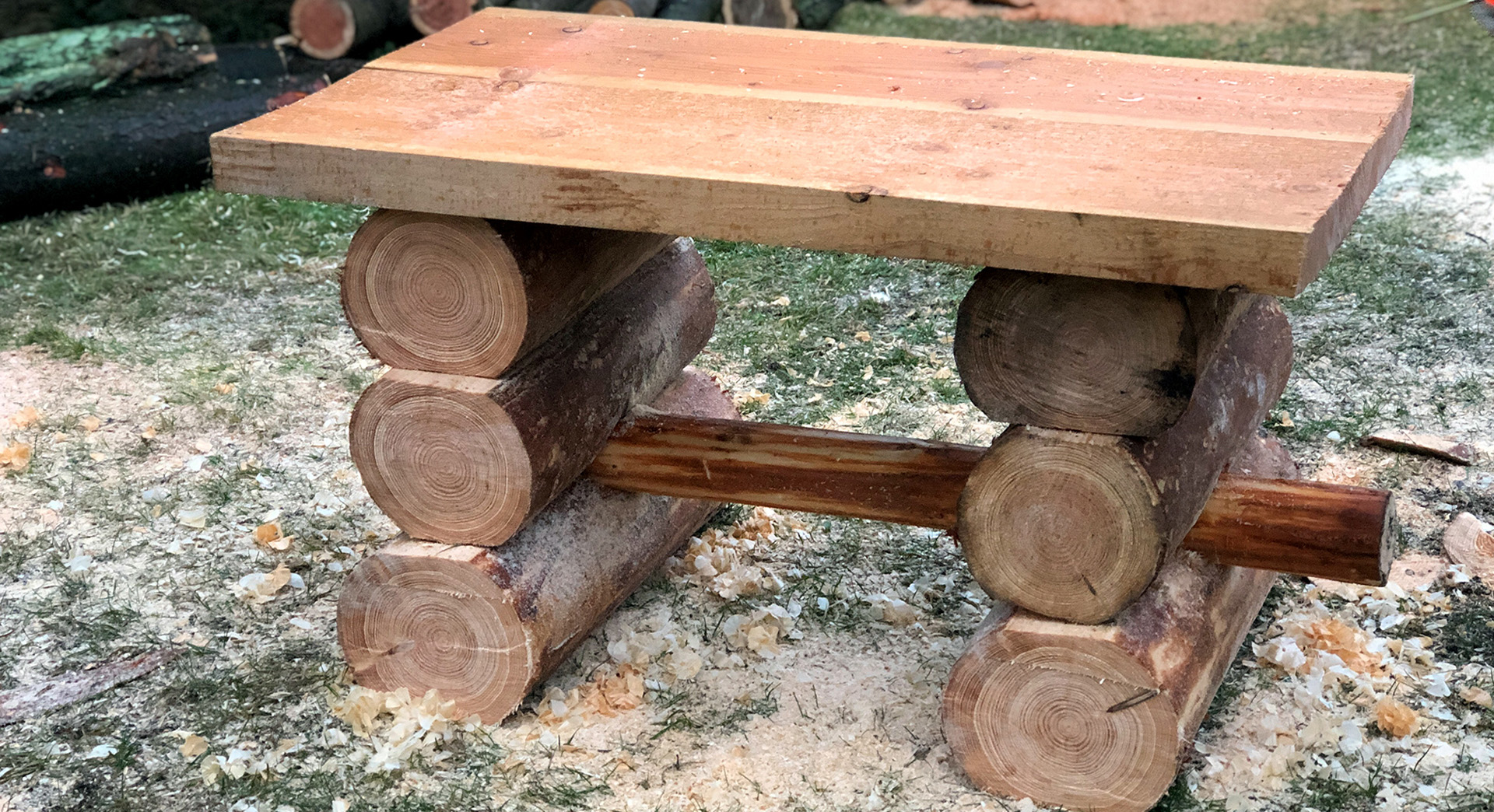 Une table de jardin en bois achevée, sur du gazon, avec de la sciure tout autour