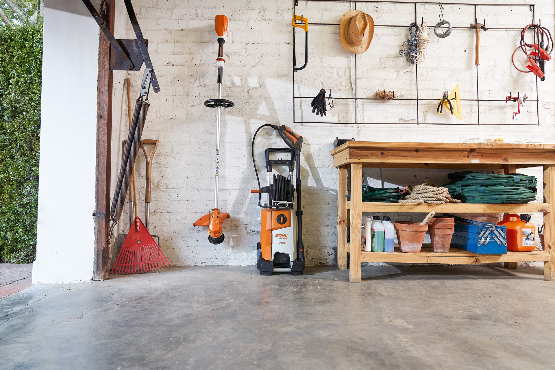 Le nettoyeur haute pression STIHL RE 130 plus et une débroussailleuse STIHL entreposés avec des outils de jardin dans un garage 