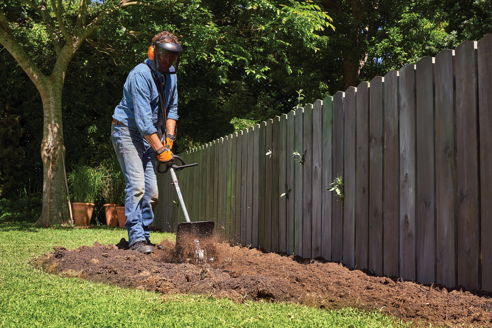 Een persoon met persoonlijke beschermingsmiddelen, cultiveert grond in een tuin met een STIHL CombiSysteem met pikhaak