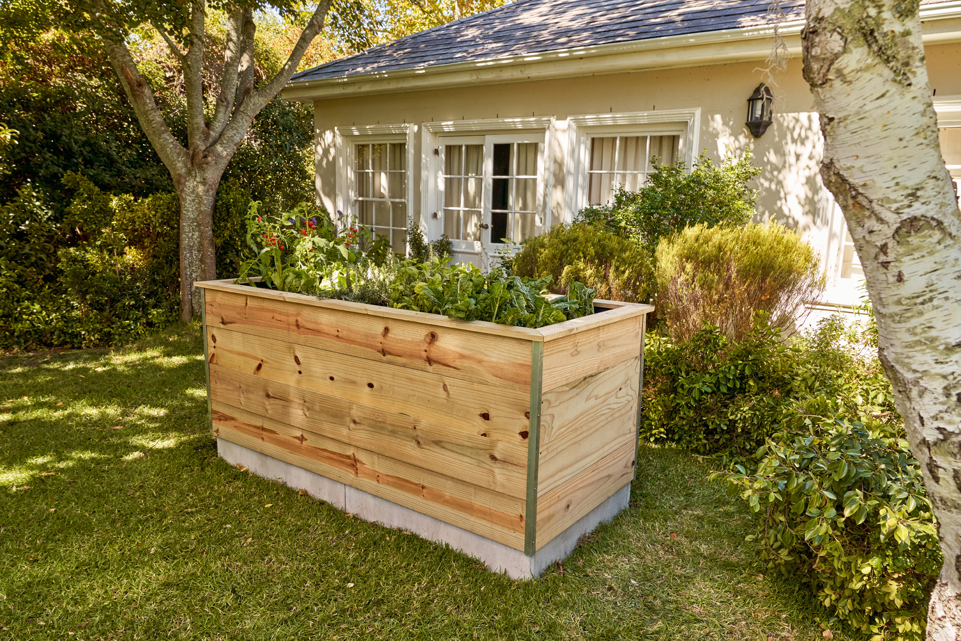 Een zelfgemaakt, verhoogd houten kweekbed staat in de tuin voor een huis