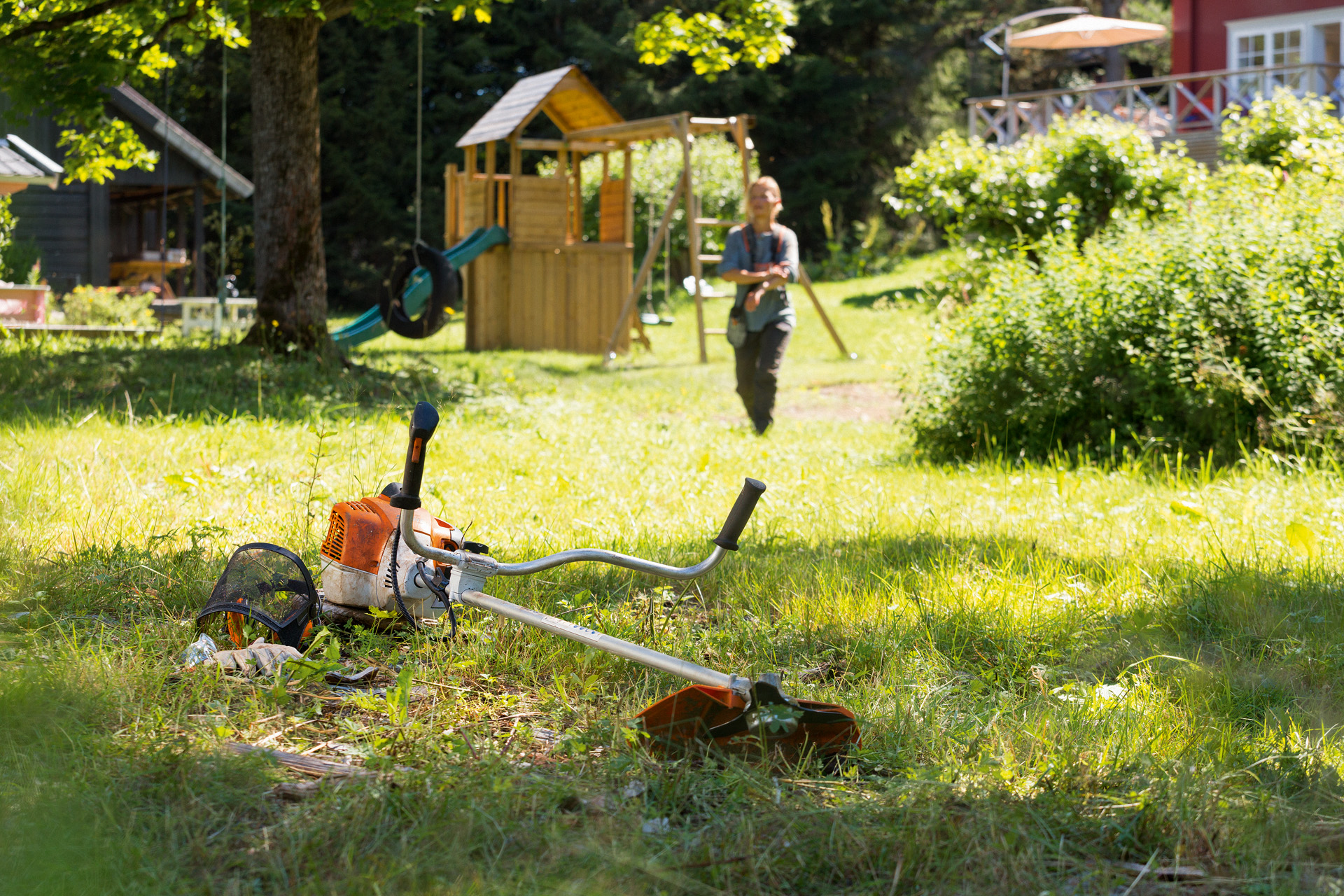 La débroussailleuse STIHL FS240 est posée dans l’herbe, un homme se prépare à l’entretien en arrière-plan