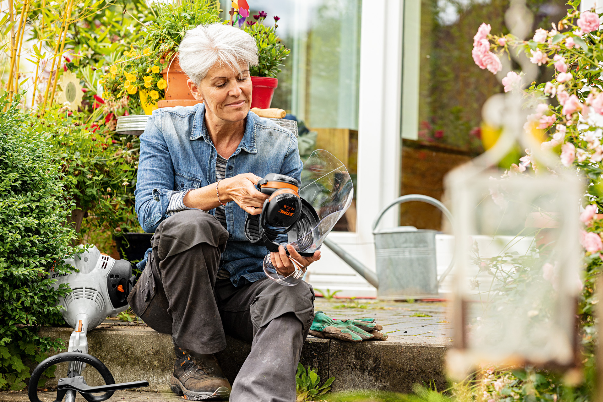 Vrouw zit tussen bloeiende planten naast een STIHL FS 38 grastrimmer en bekijkt de veiligheidsuitrusting