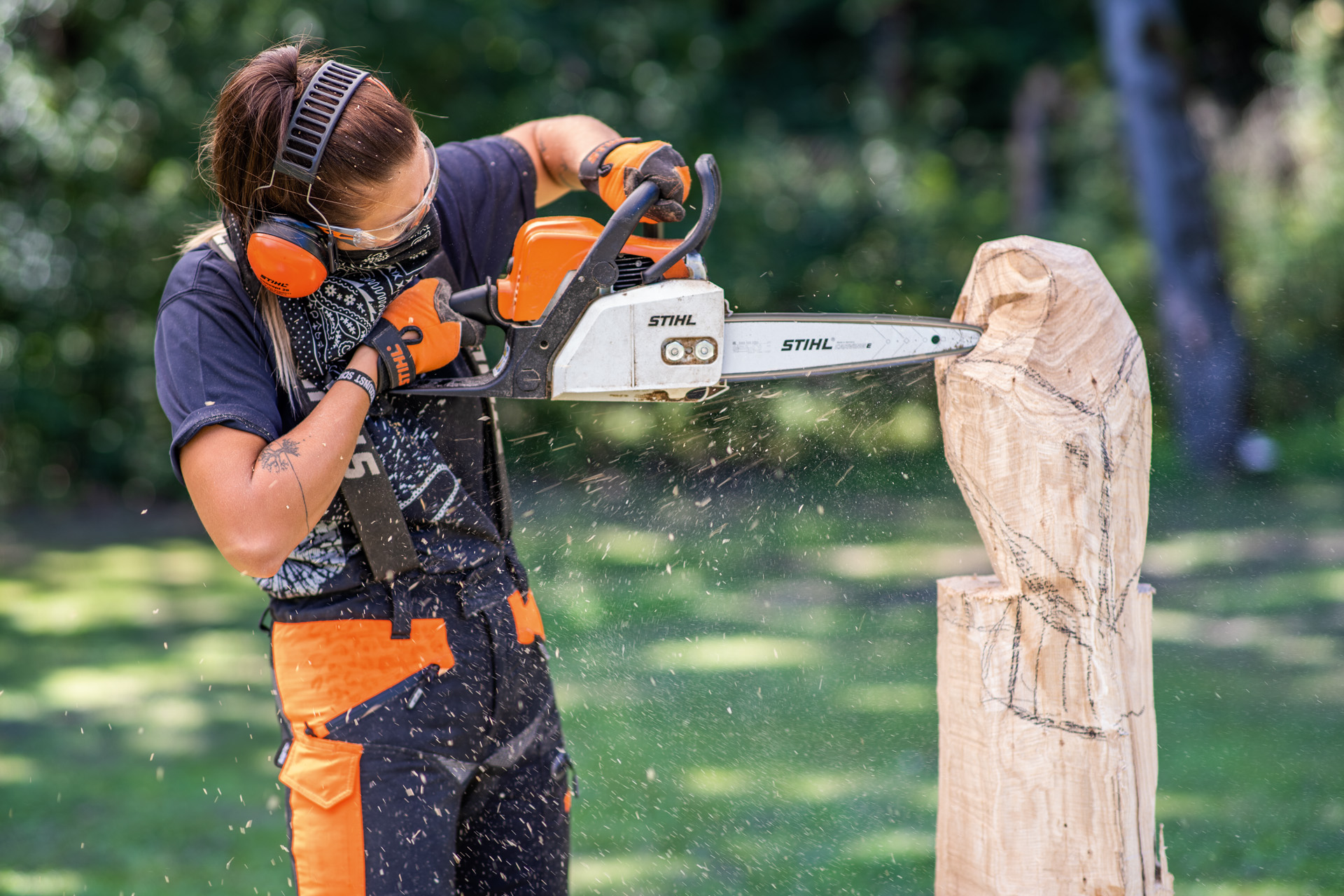 Vrouw met gehoorbescherming maakt een houten uil met de kettingzaag