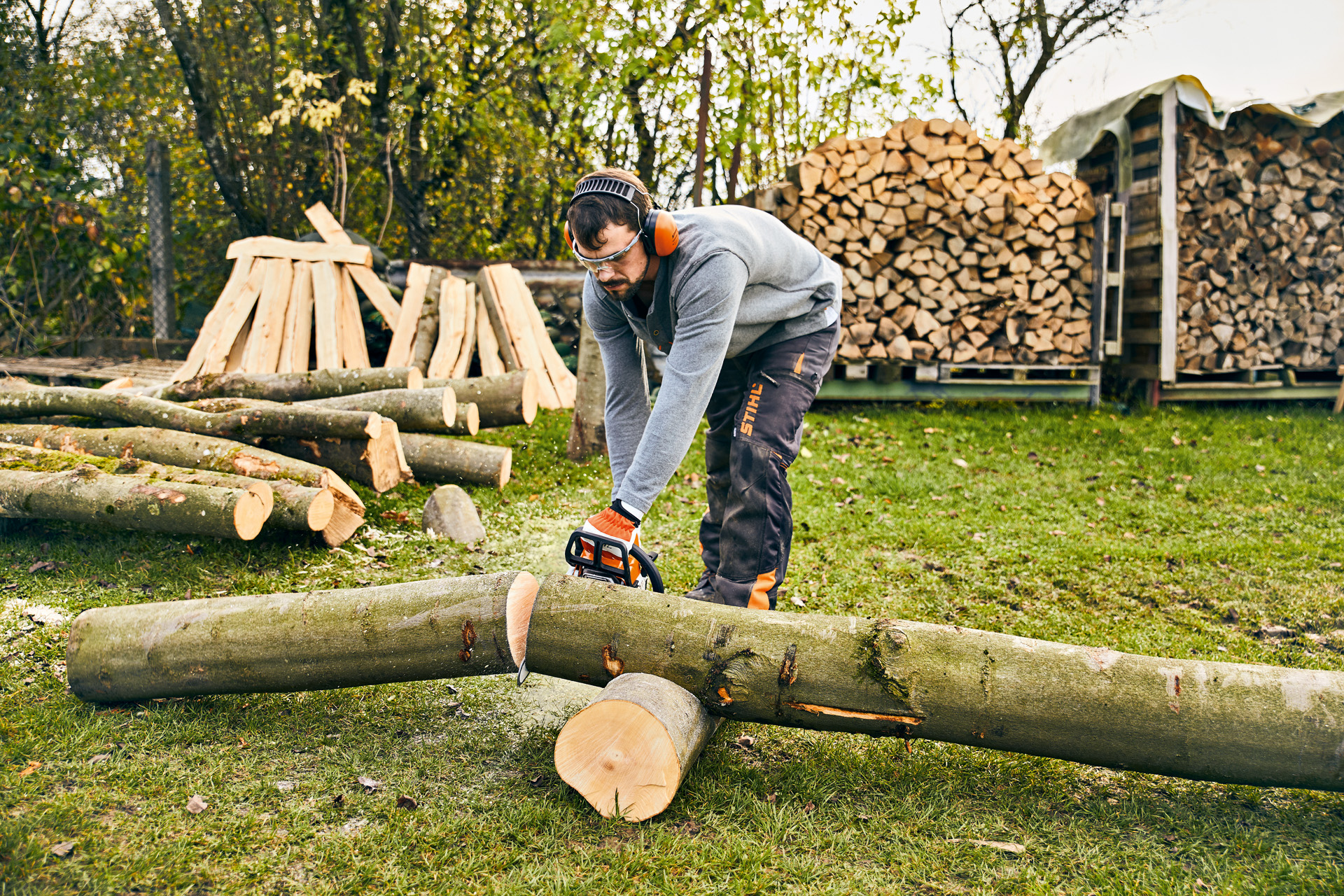 Man met veiligheidsbril en gehoorbescherming zaagt een boomstam met een STIHL benzine-kettingzaag MS 180