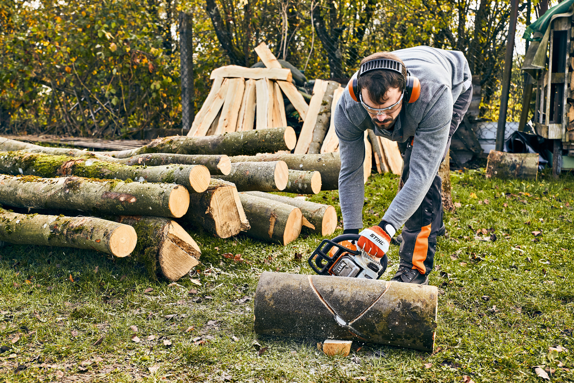 Un homme avec protections auditives, utilise la tronçonneuse STIHL MS 180 pour fabriquer un banc de jardin en bois