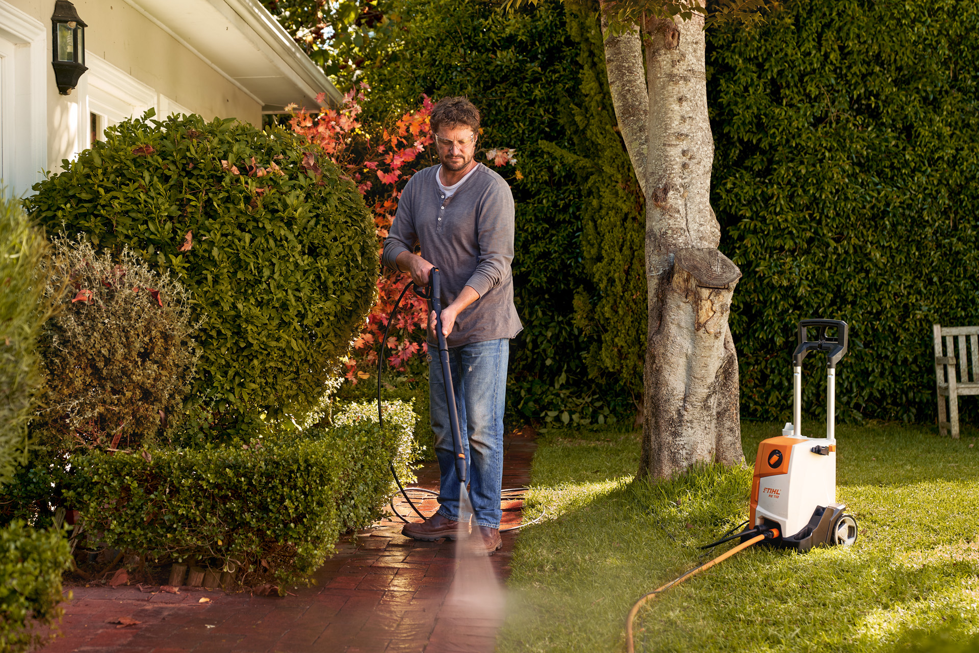 Een man die de tegels voor zijn huis schoonmaakt met een STIHL RE 110 hogedrukreiniger