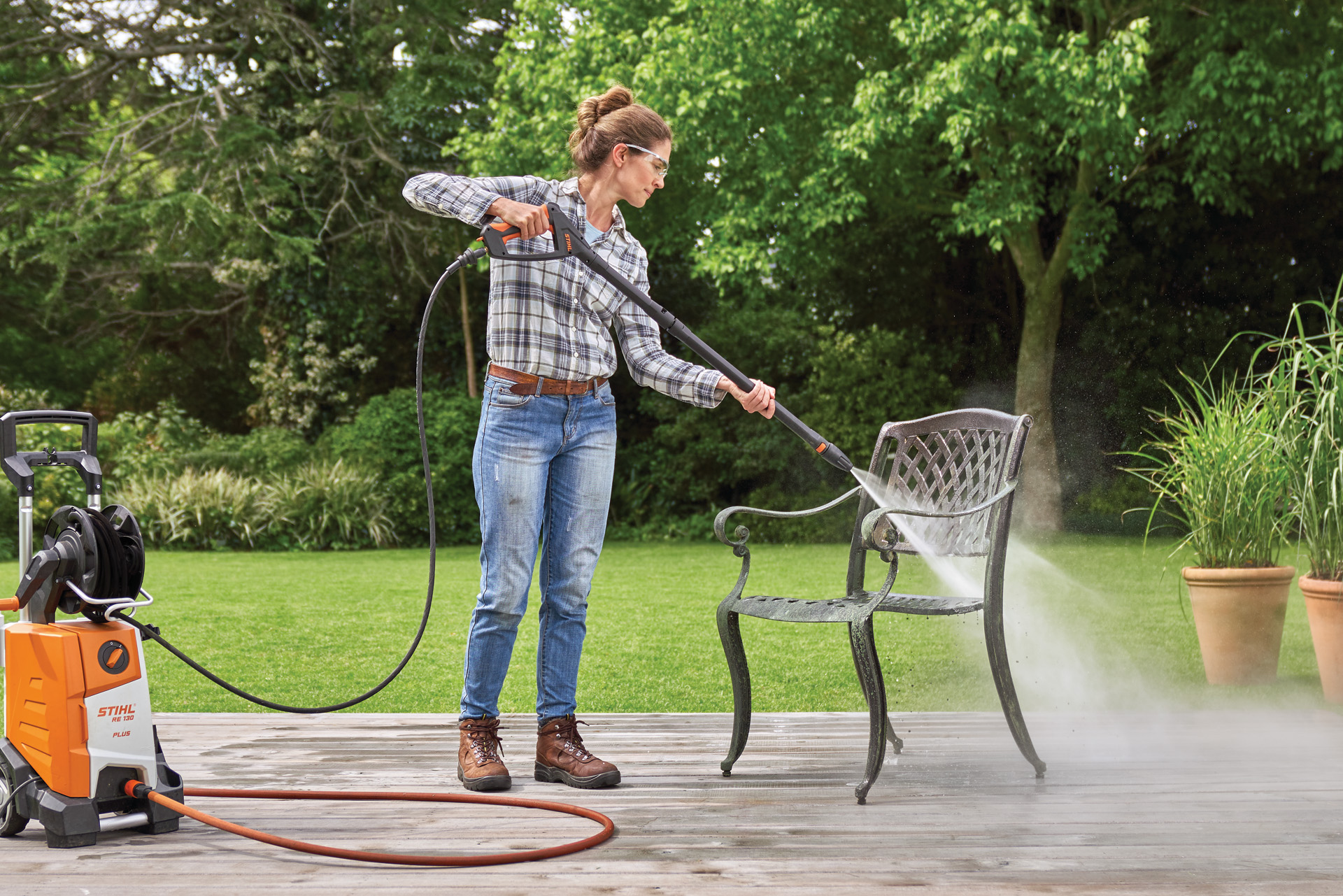 Een vrouw die de STIHL RE 130 Plus hogedrukreiniger gebruikt op een metalen stoel op een terras in een tuin