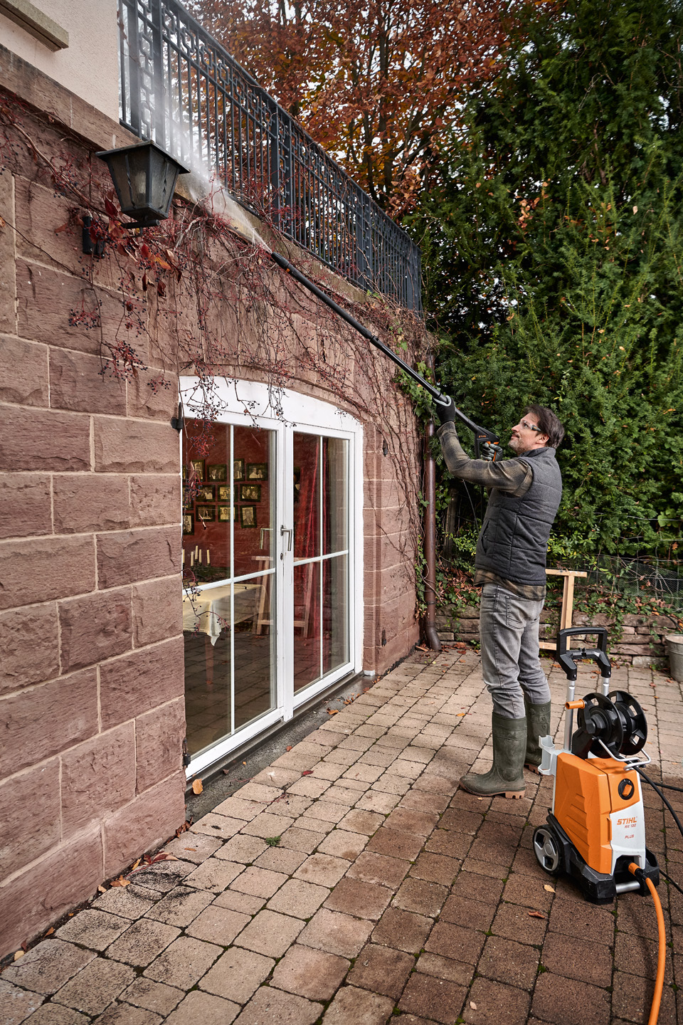 Een man die op een terras staat en de gevel van een huis schoonmaakt met een STIHL hogedrukreiniger