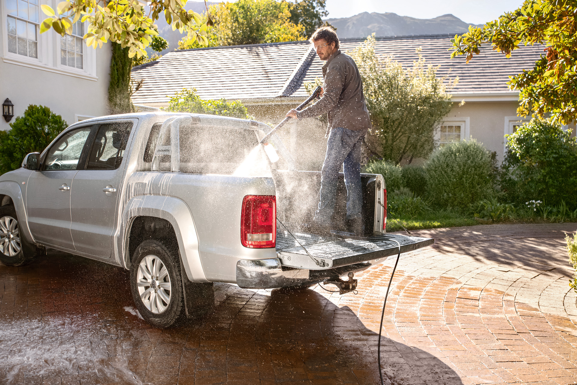 Homme debout sur le plancher d’un pick-up, nettoyant le véhicule avec un nettoyeur haute pression