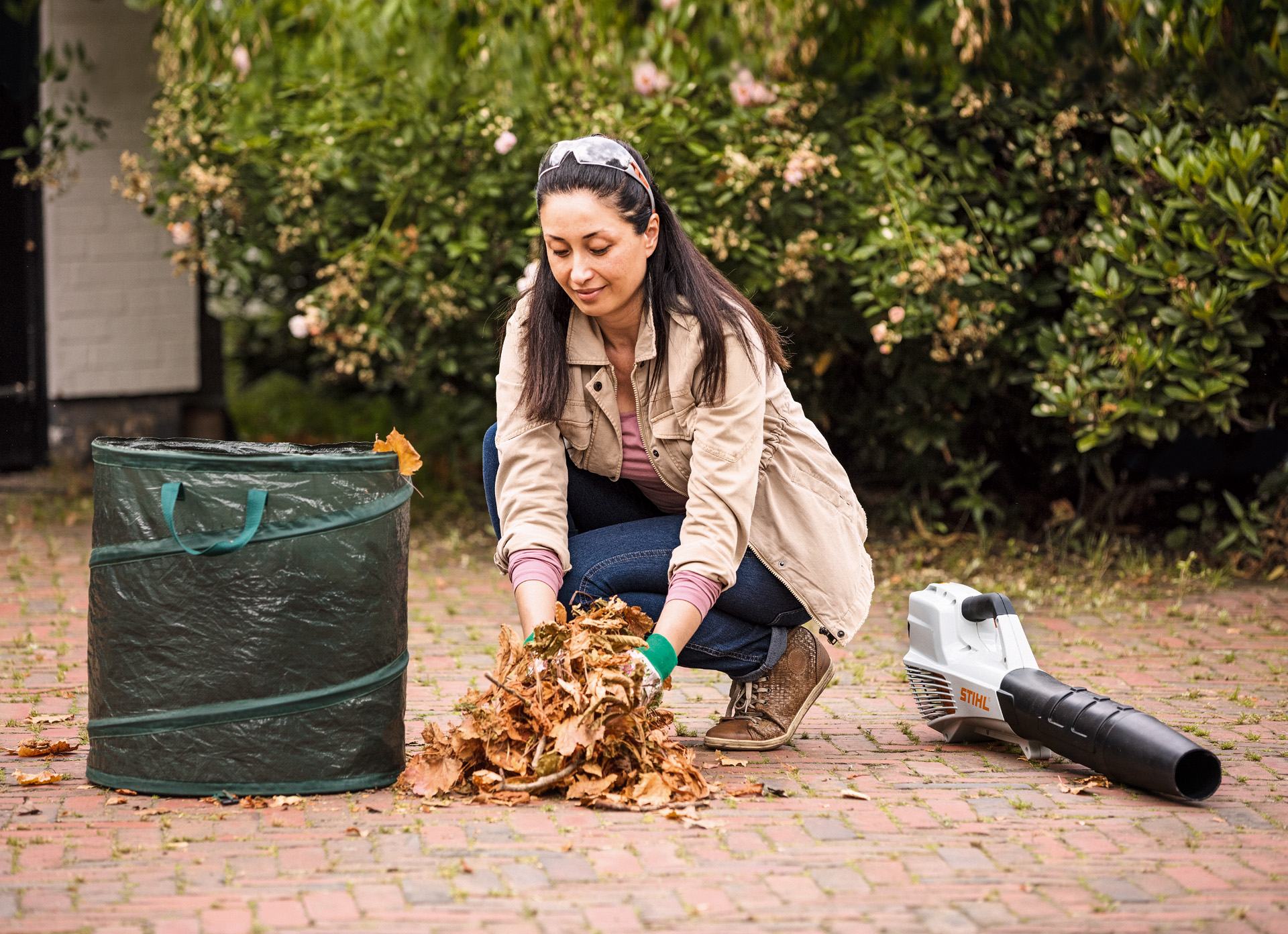 Vrouw ruimt bladeren op met een tuinafvalzak en een STIHL BGA 56 bladblazer