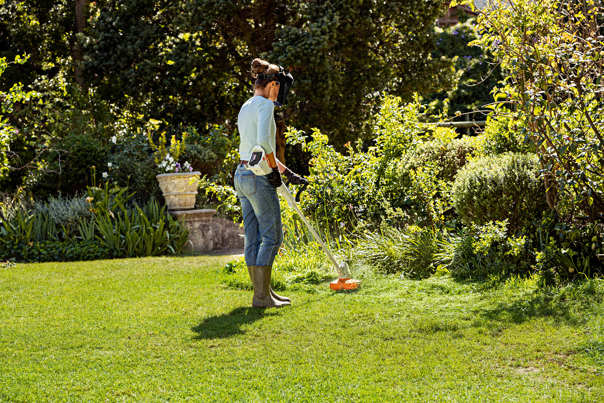 Une femme équipée d’une visière de protection et de gants utilisant un coupe-bordure STIHL FSA 56 à batterie dans un jardin