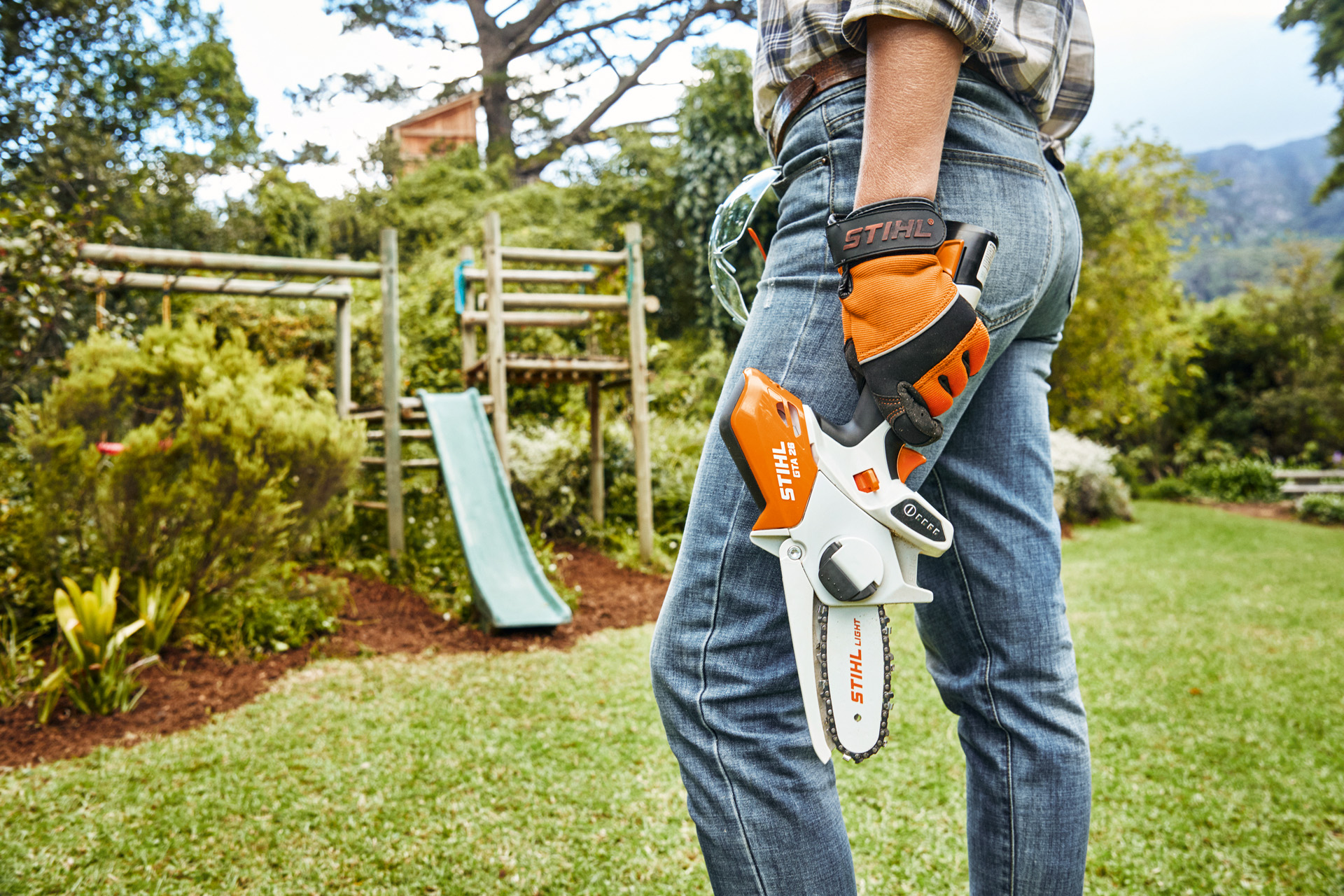 Persoon met STIHL GTA26 accusnoeizaag staat in de tuin voor een glijbaan