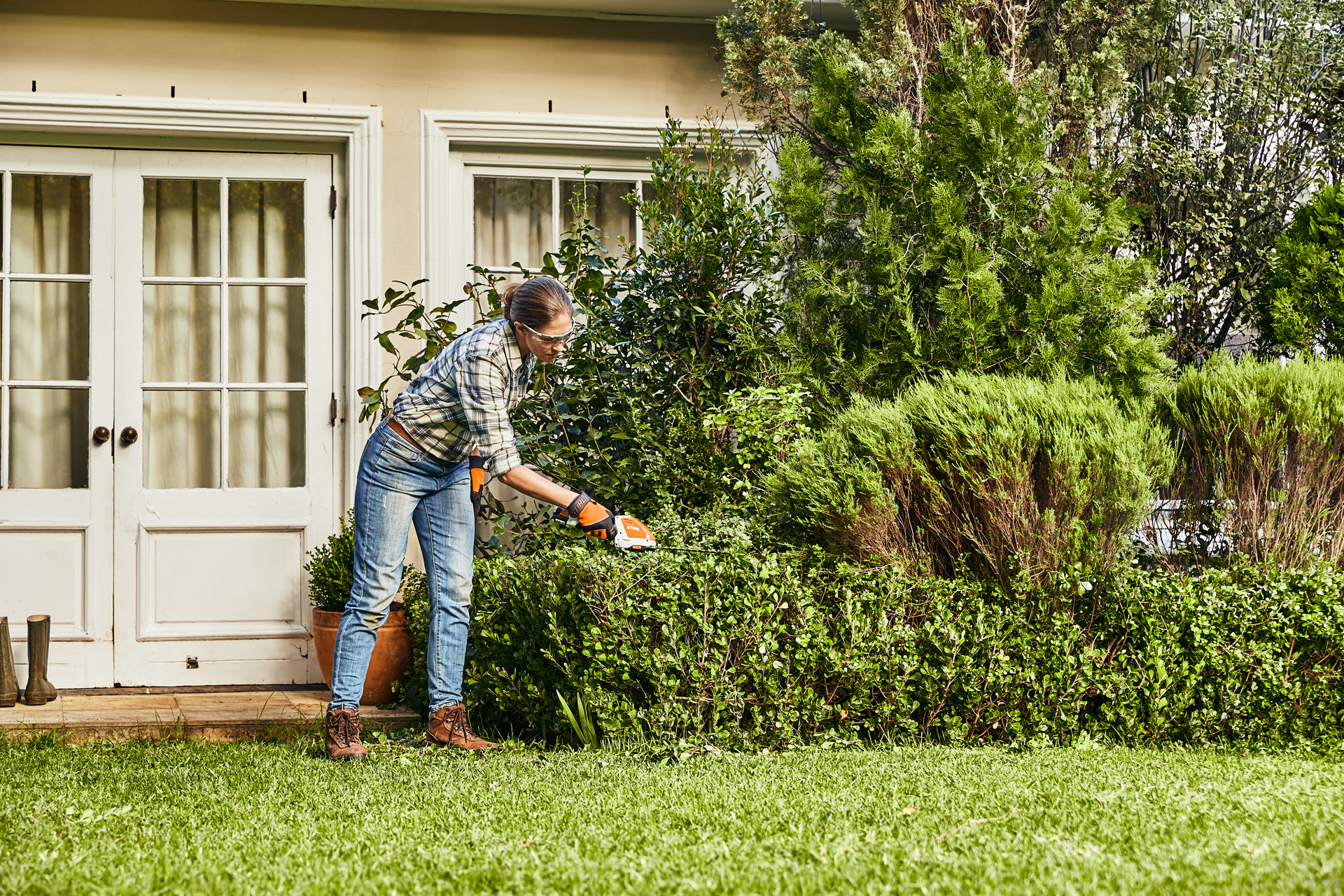 Vrouw die een buxushaag voor een wit huis snoeit met een STIHL HSA 26 accuheggenschaar