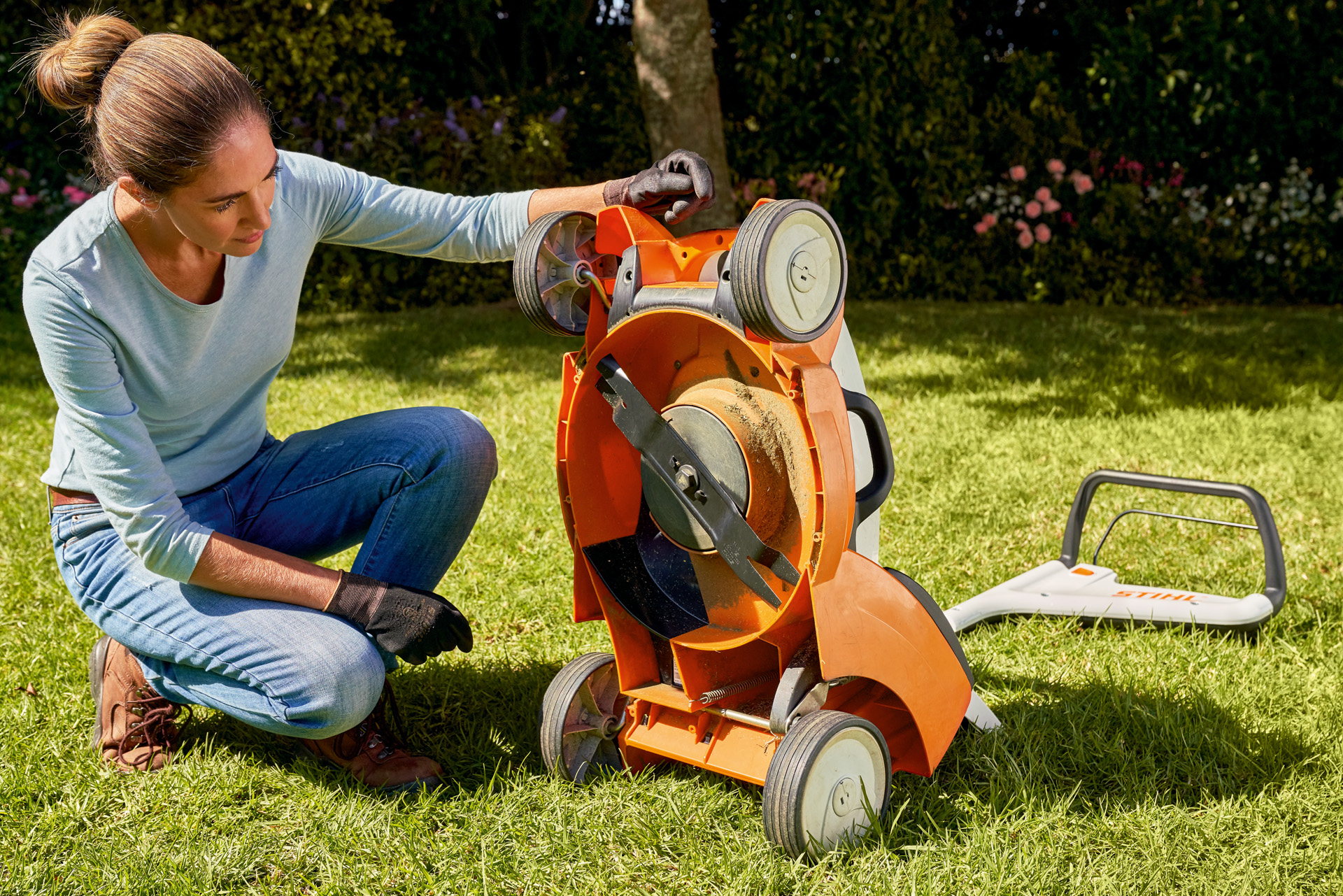 Een vrouw bekijkt de onderkant van een STIHL RMA 339C accugrasmaaier