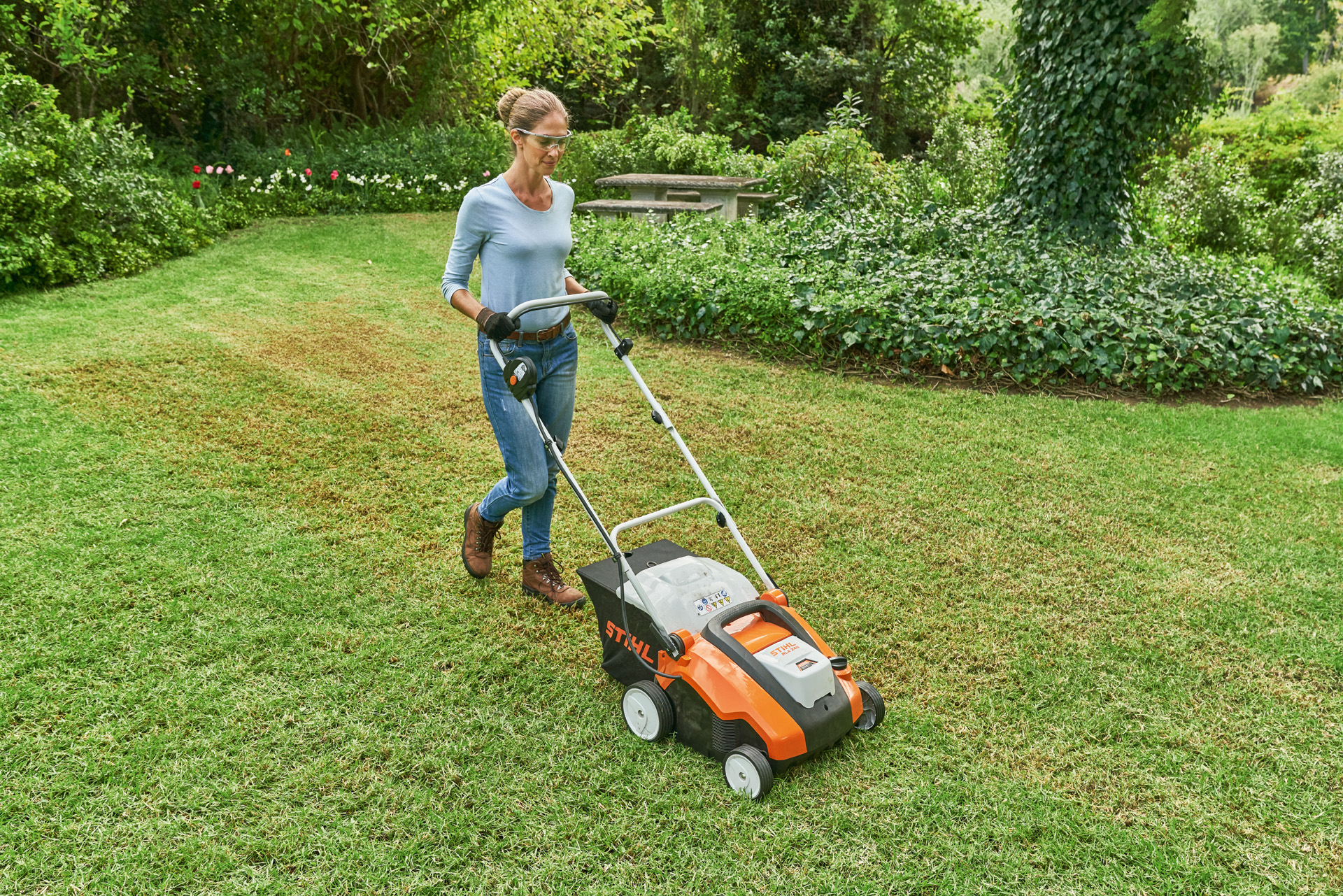 Vrouw met veiligheidsbril en werkhandschoenen verticuteert een klein gazon met de STIHL accuverticuteermachines RLA 240.