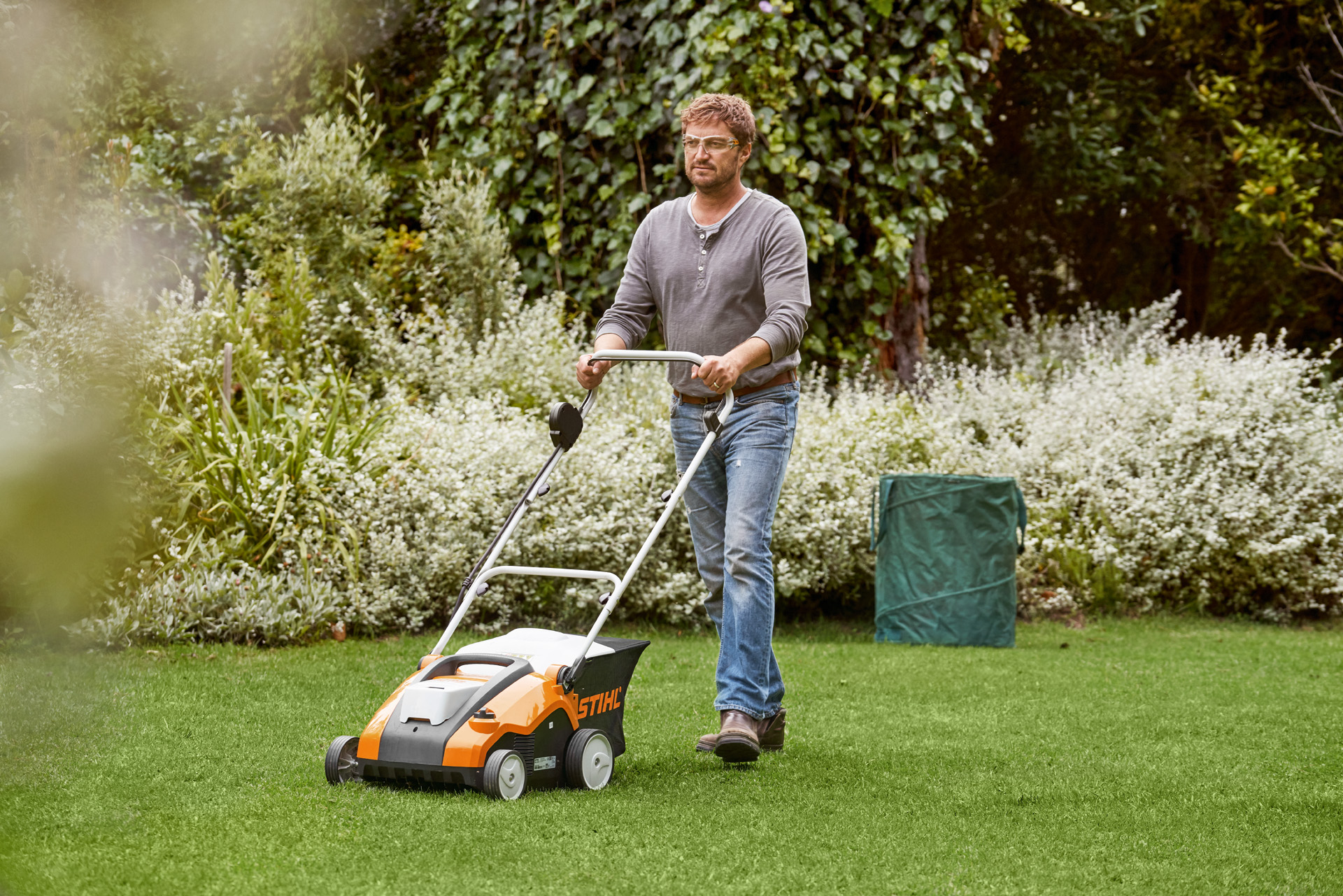 Une homme utilise le scarificateur électrique STIHL RLE 240 pour scarifier une pelouse entourée d’arbres et d’arbustes verts