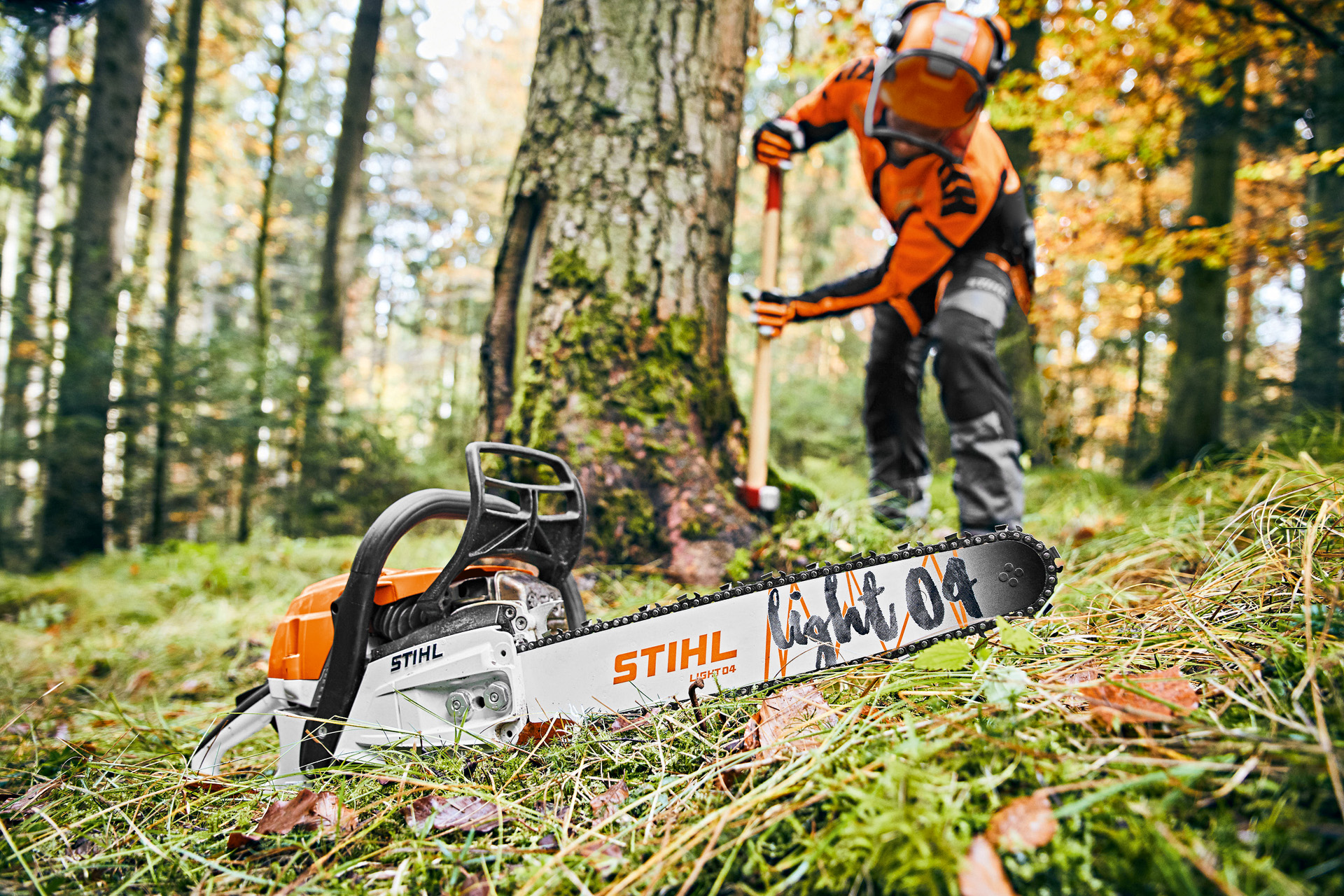 Homme dans la forêt portant un équipement de protection avec, au premier plan, une tronçonneuse thermique équipée du guide Light 04