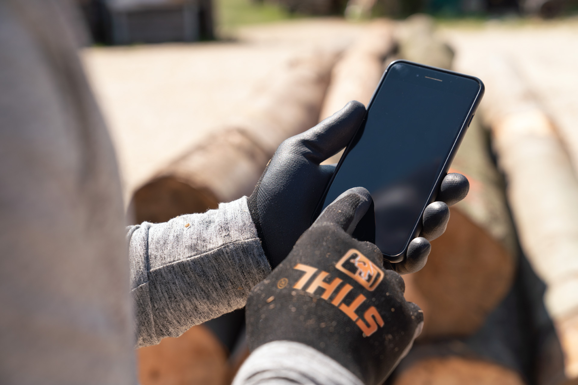 Een man met STIHL veiligheidshandschoenen tikt op zijn smartphone