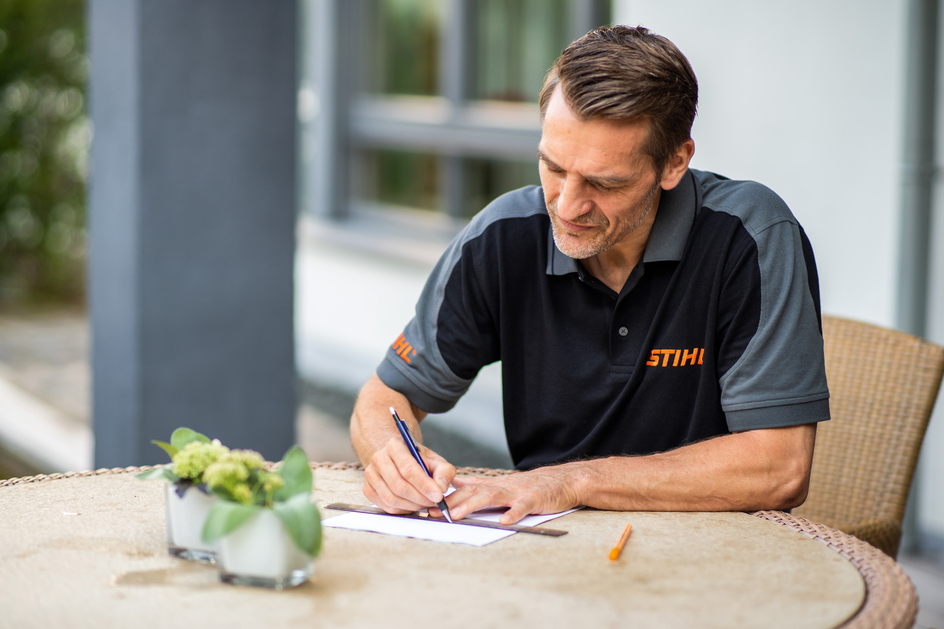 Le revendeur STIHL s'assied à la table de jardin et dessine le plan de la pelouse qui sera tondue par le robot de tonte iMOW.