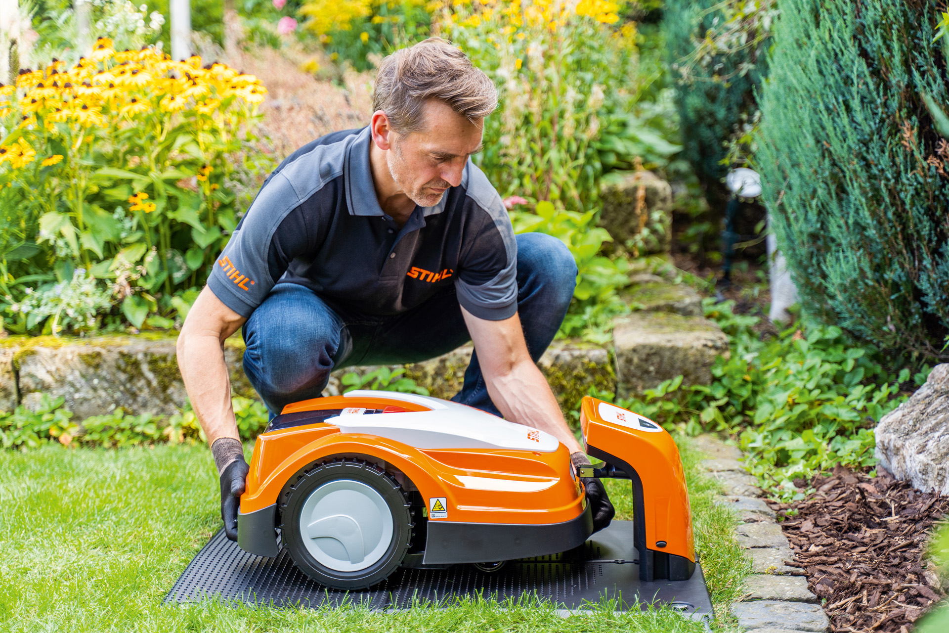 STIHL dealer plaatst een STIHL iMOW robotmaaier in zijn laadstation in een tuin