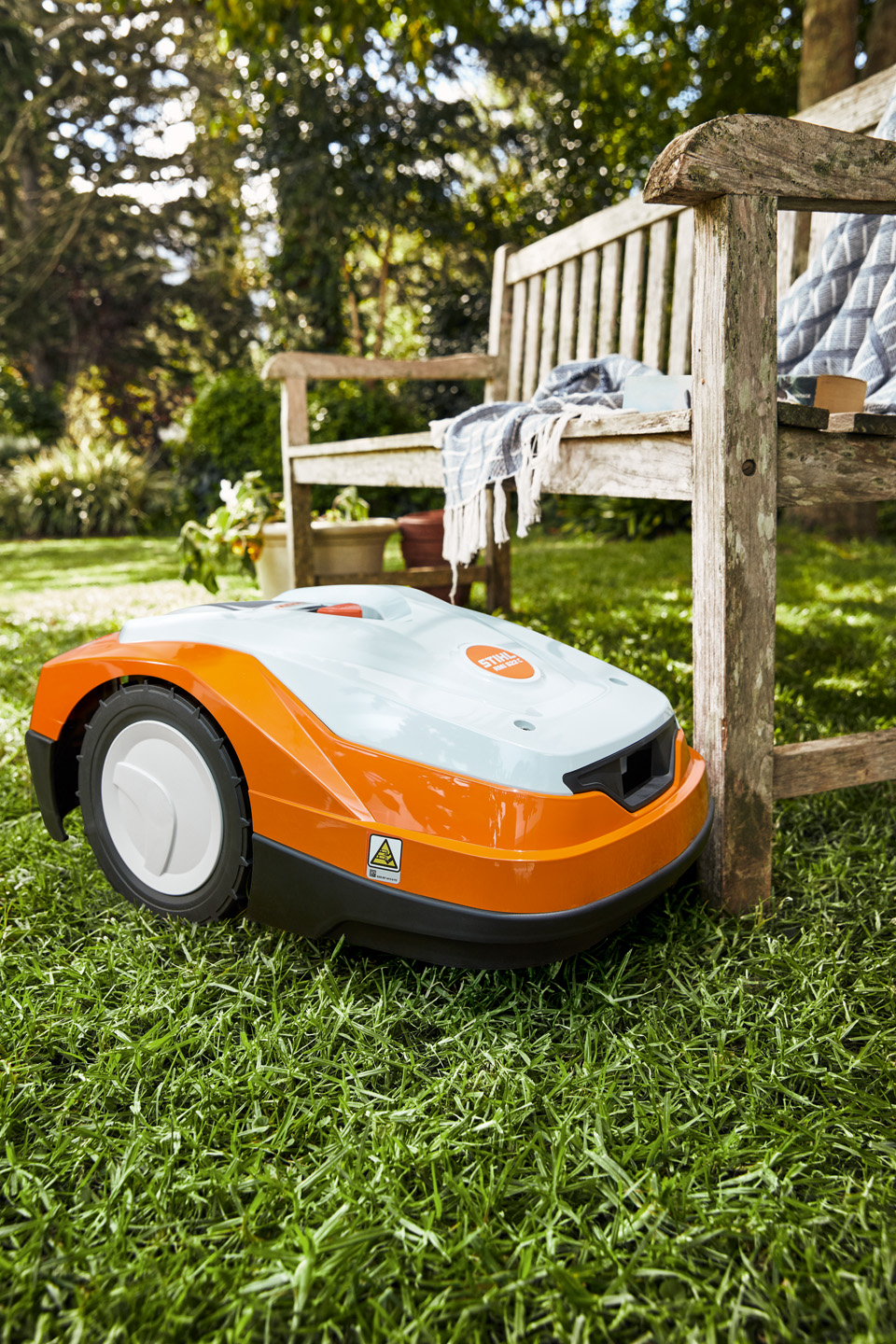 A STIHL iMOW® RM 522 robot mower on a green lawn beside a bench