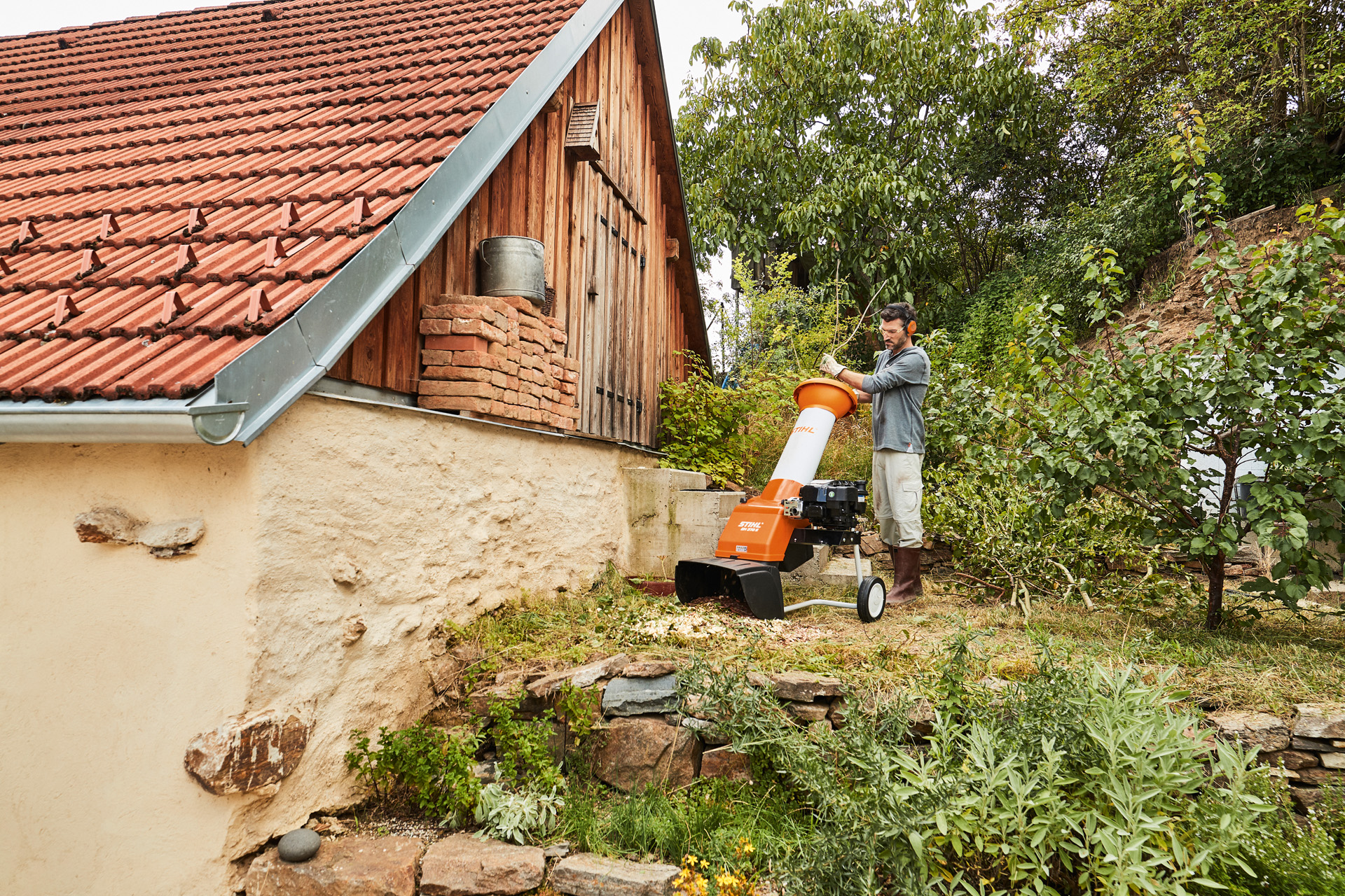 Man met STIHL benzinehakselaar naast bomen en struiken voor een huis