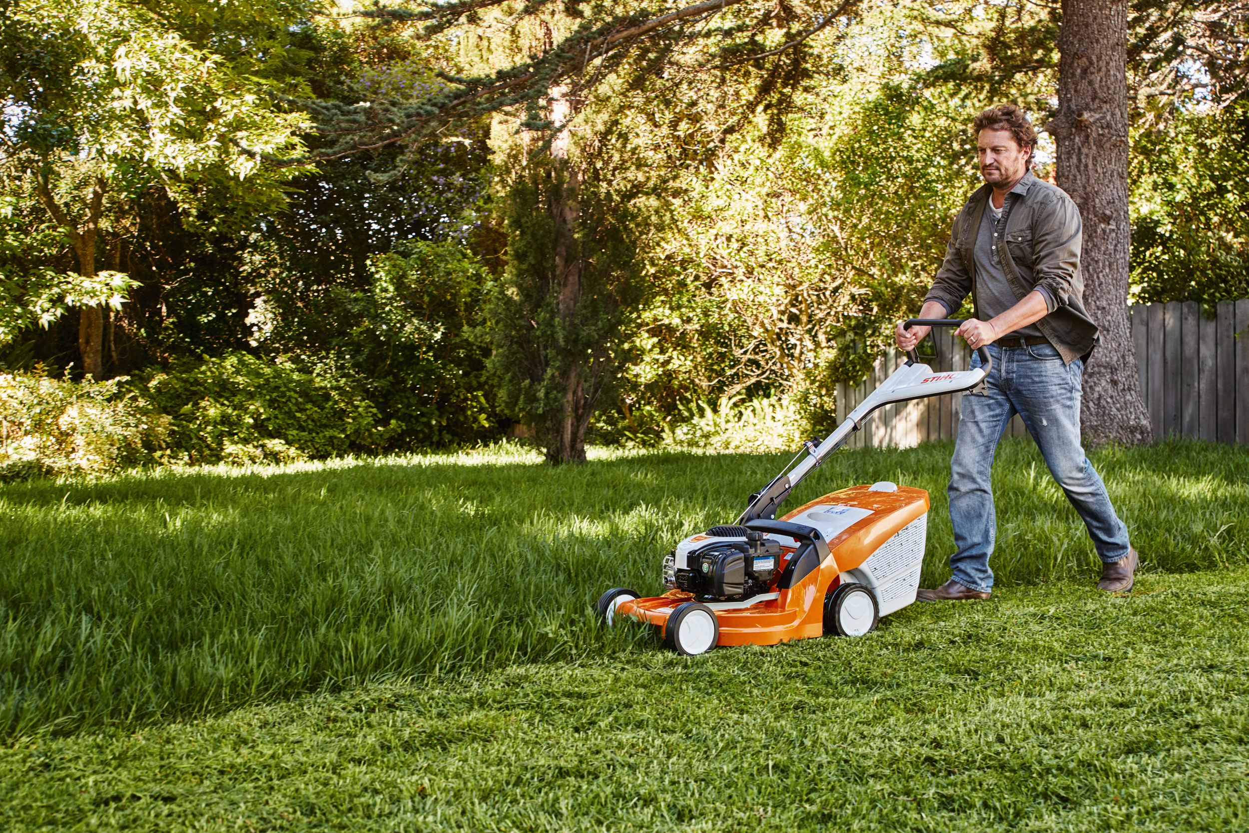 Een man maait het gras in een tuin met een STIHL grasmaaier