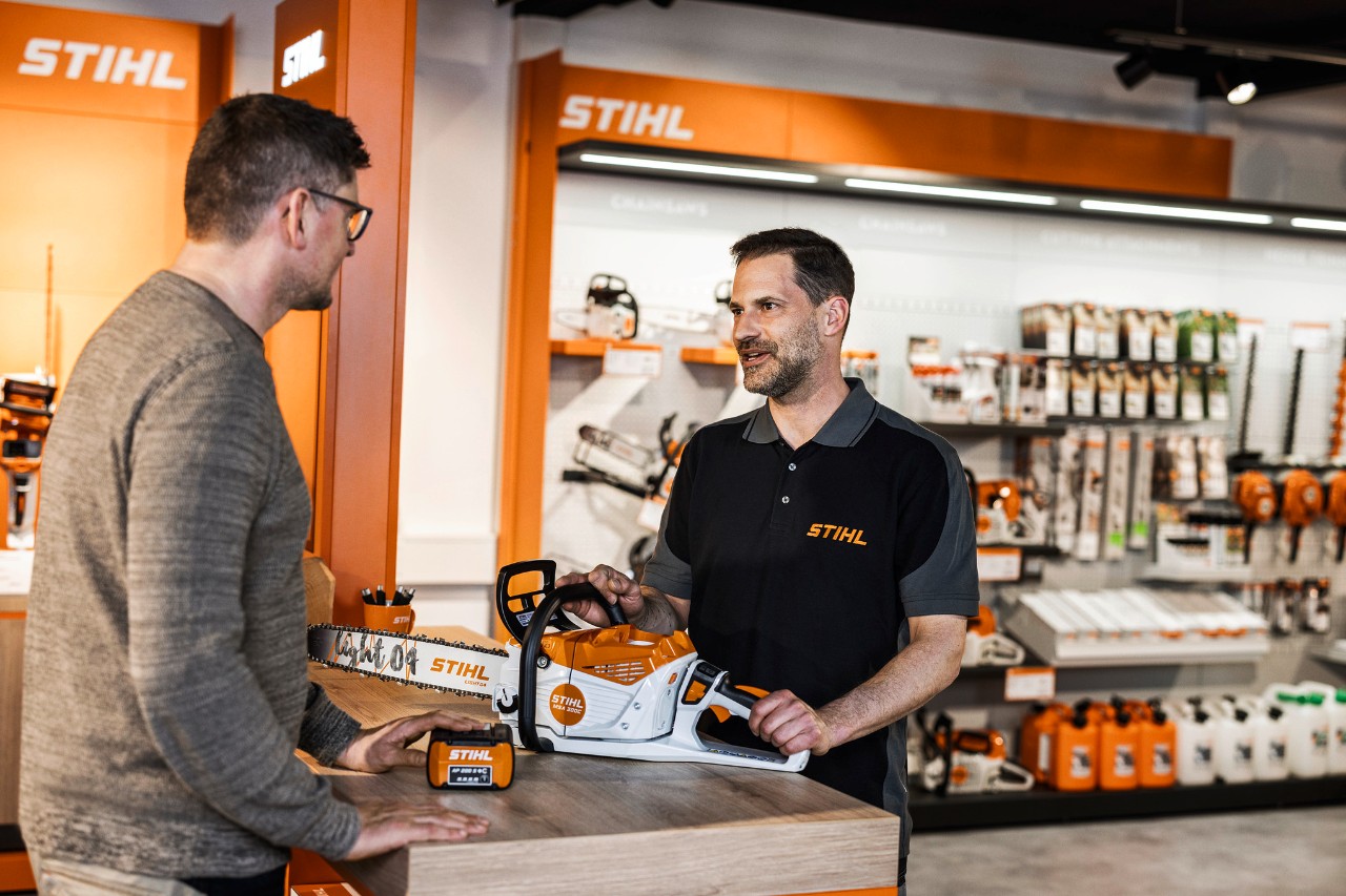 Un revendeur STIHL conseille ses clients sur la tronçonneuse sans fil STIHL MSA 300 dans sa salle d'exposition.