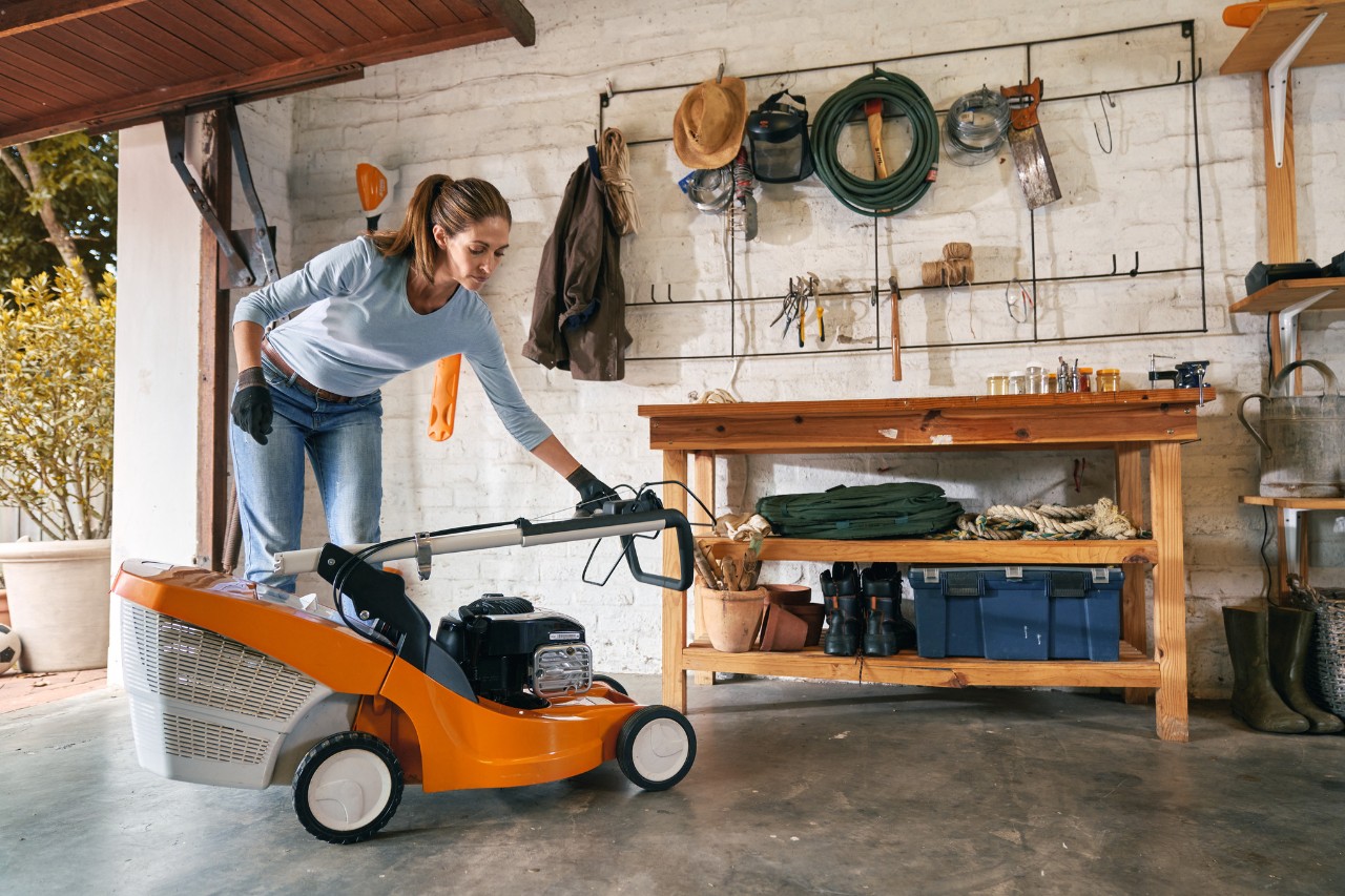 A woman stands in a garage and folds up a lawnmower