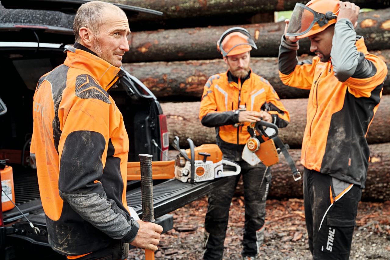 Drie mannen in beschermende uitrusting voor een voertuig met geopende bagageruimte vol met STIHL accumachines