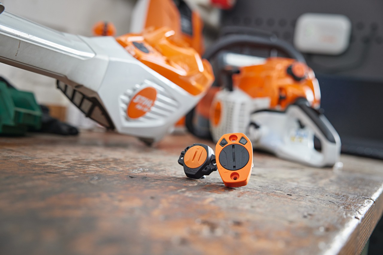 Een STIHL Smart Connector en een STIHL Smart Connector 2 A liggen op een werkbank met andere STIHL machines erachter.