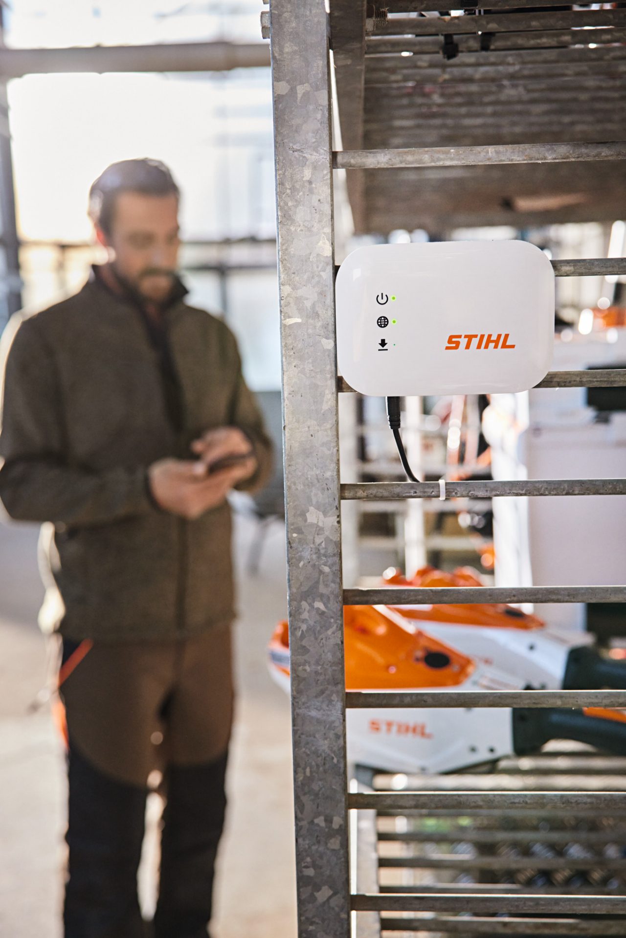 Een STIHL connected Box hangt aan een rek in een werkplaats. Op de achtergrond staat een tuin- en landschapsarchitect 