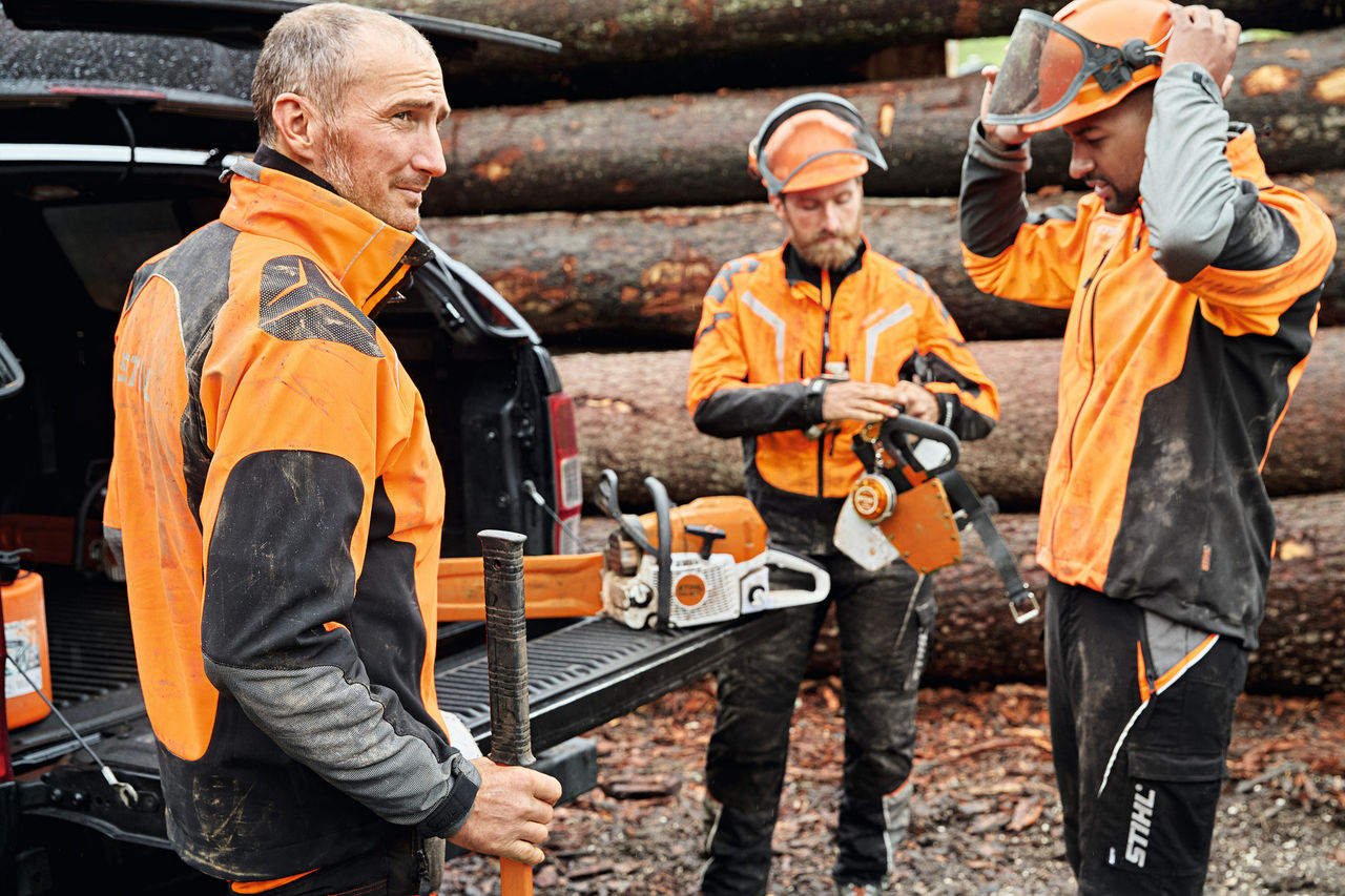 Drie mannen in STIHL veiligheidsuitrusting met STIHL accumachines voor de laadvloer van een auto