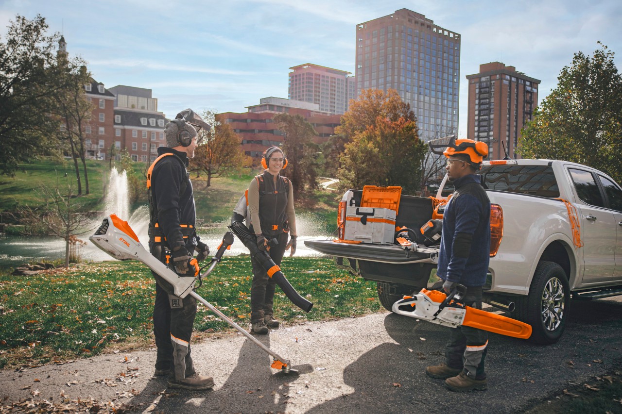 Een groep professionele tuinarchitecten die bij hun voertuigen staan en zich met accugereedschap van STIHL klaarmaken voor het werk.