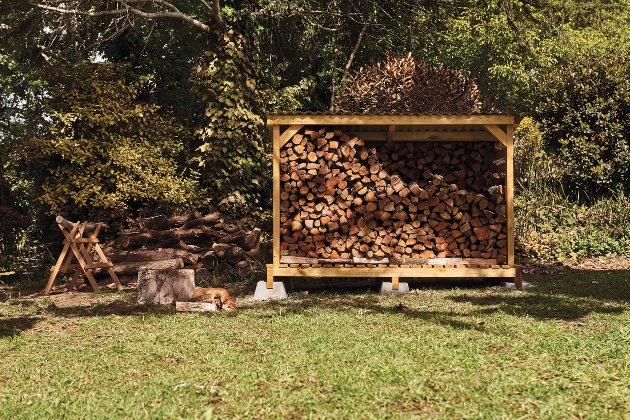 Zelfgemaakt houten schuurtje op een tuinperceel, gevuld met houtblokken.