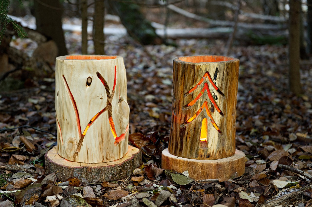 Twee houten lantaarns, de ene met een lijnmotief, de andere met een uitgesneden dennenboom.