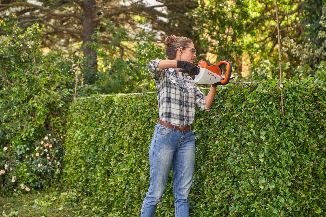 Een vrouw snoeit met de STIHL HSA 45 accuheggenschaar een heg in vorm