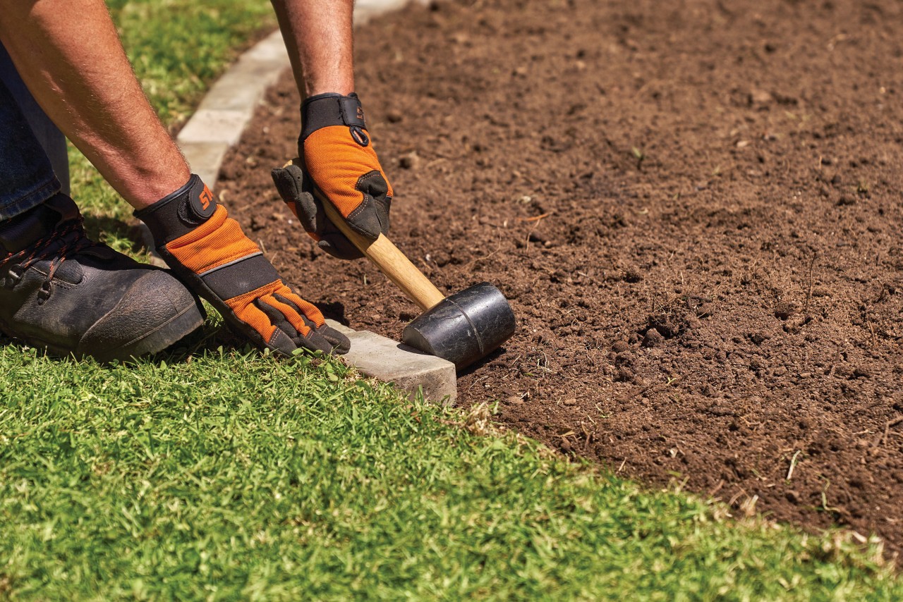 Een man klopt stenen langs een grasrand om een afboording te maken 